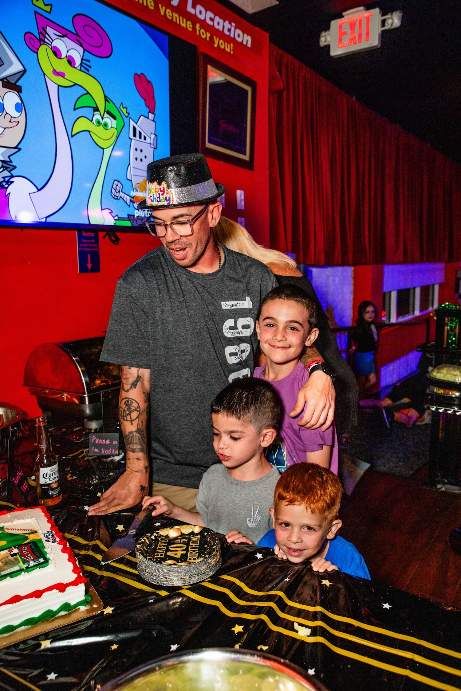 A man with tattoos is shown playing drums with children in a colorful and lively setting.