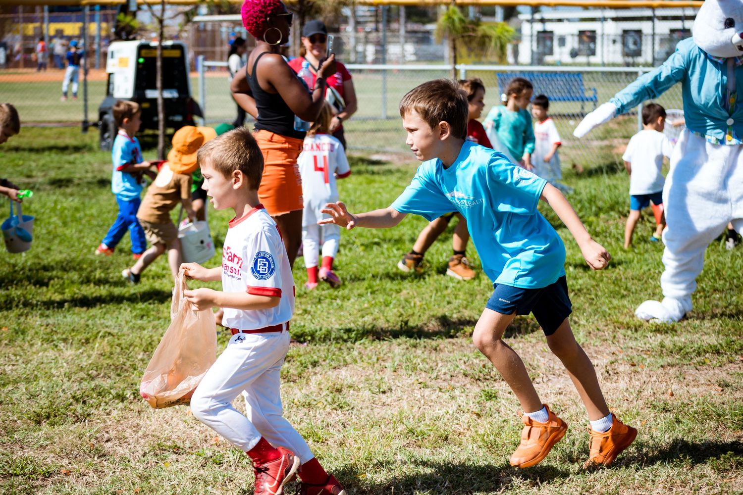 Children participate in an outdoor running activity on a sunny day in a grassy field during a youth sports event.
