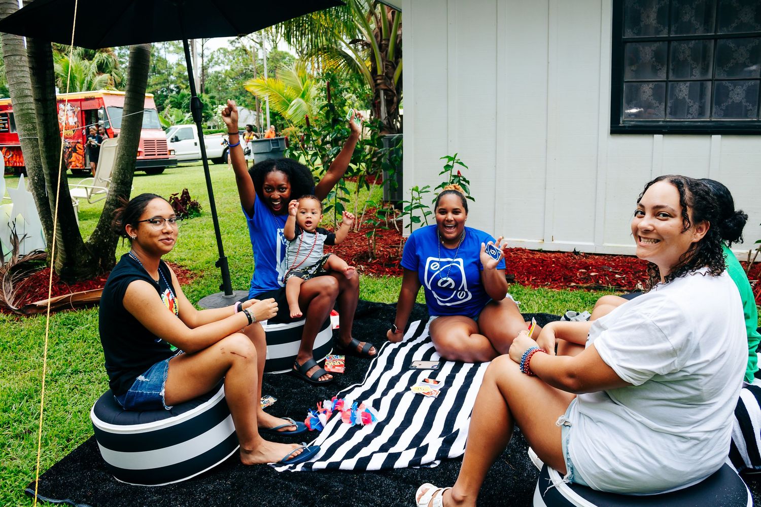 Group relaxing on striped outdoor seating during backyard party.
