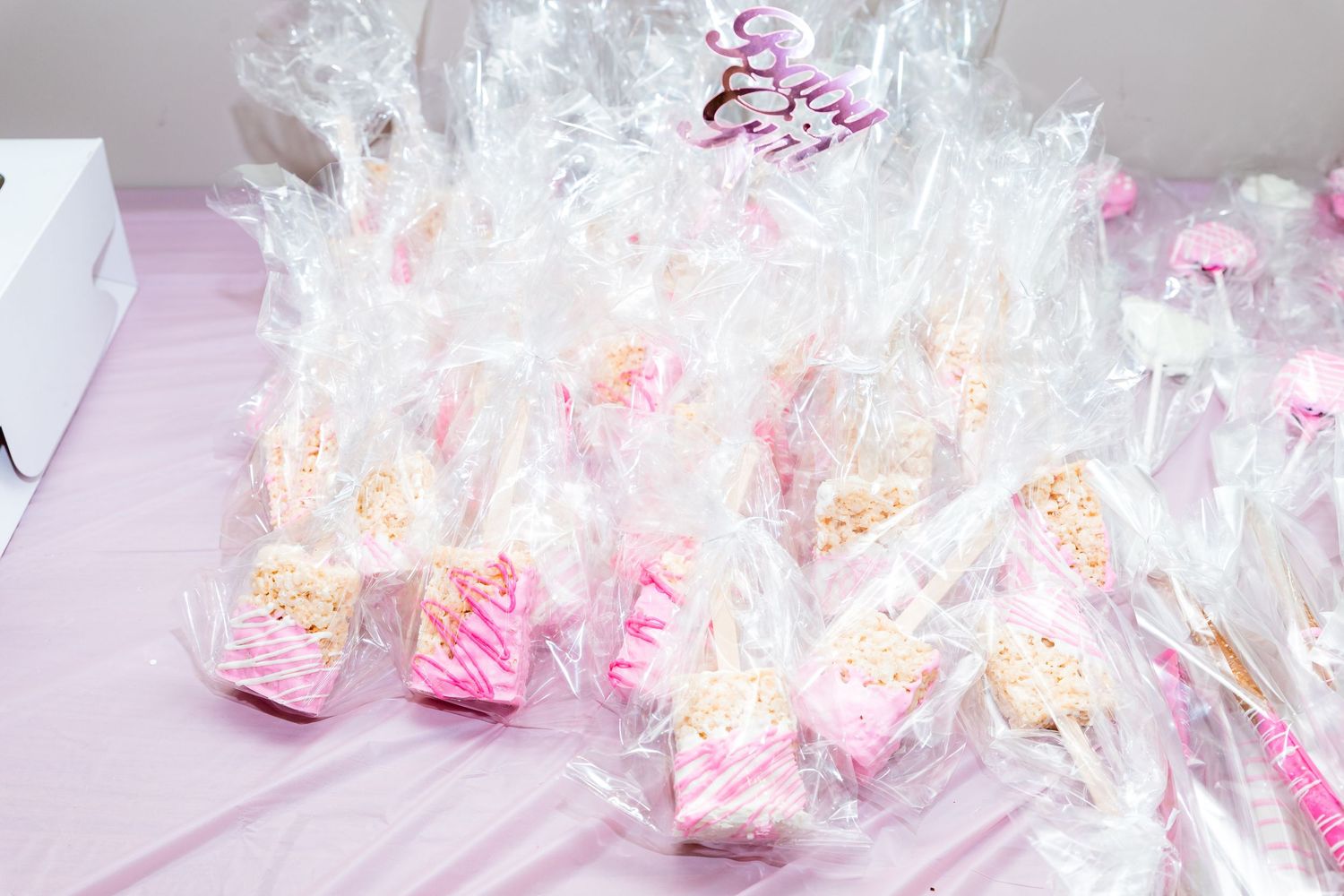 Pink and white party favors wrapped in clear cellophane bags arranged in rows on a light pink surface.