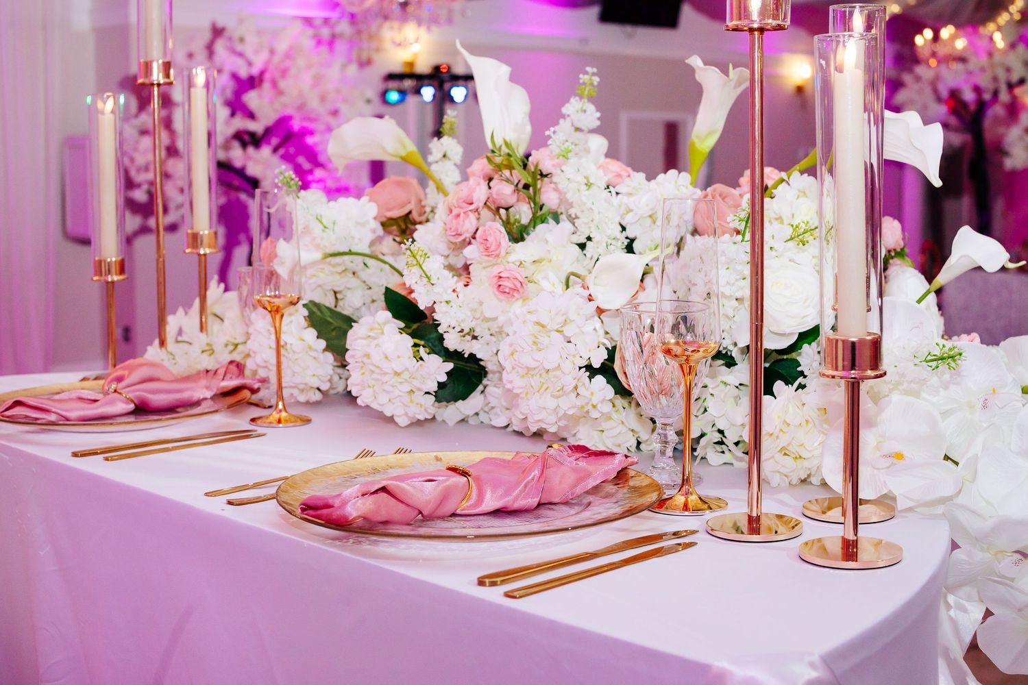 Wedding reception table settings with pink florals, gold accents, and elegant white linens.