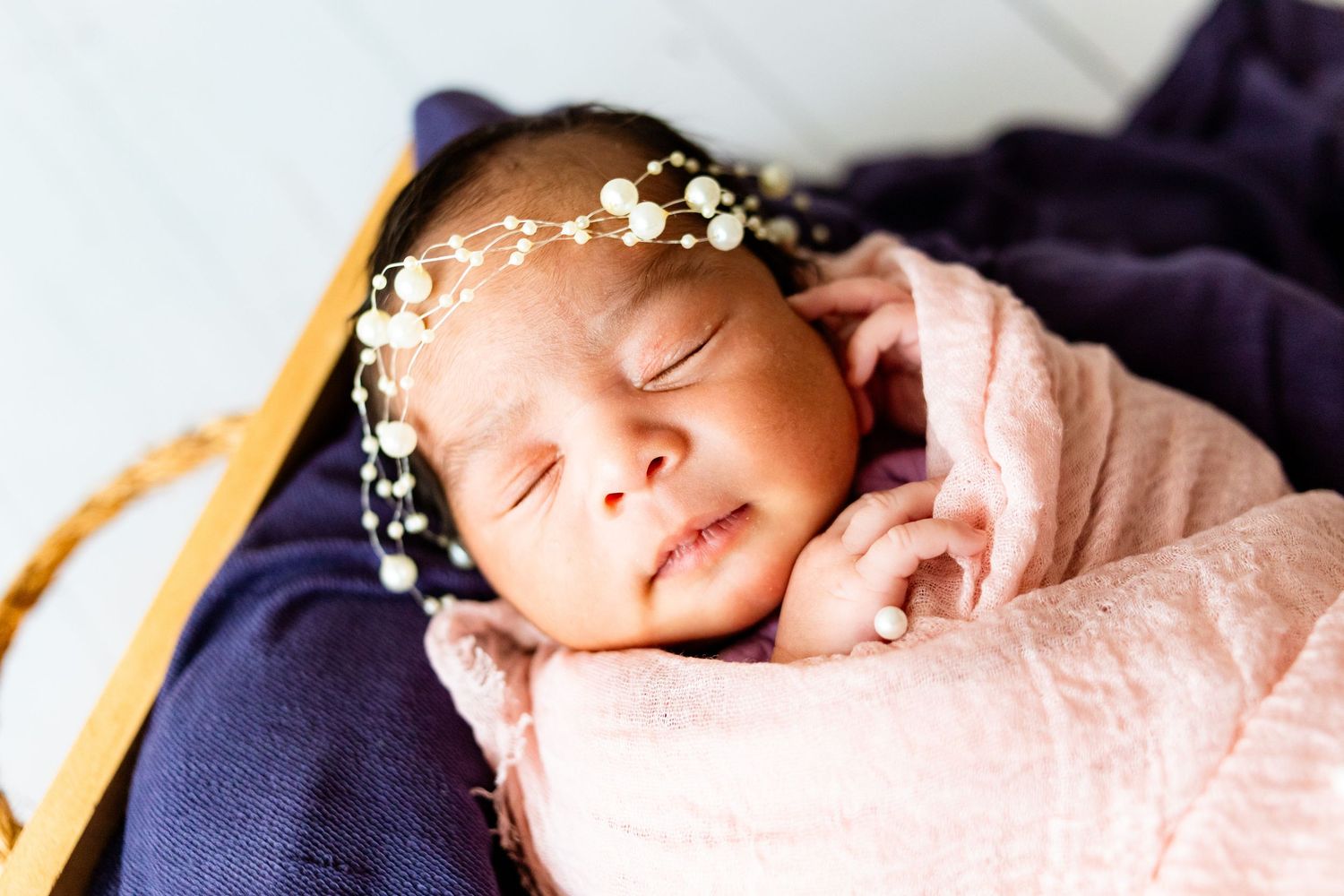 Close-up of a peaceful sleeping newborn wearing a delicate floral headband wrapped in pink cloth.