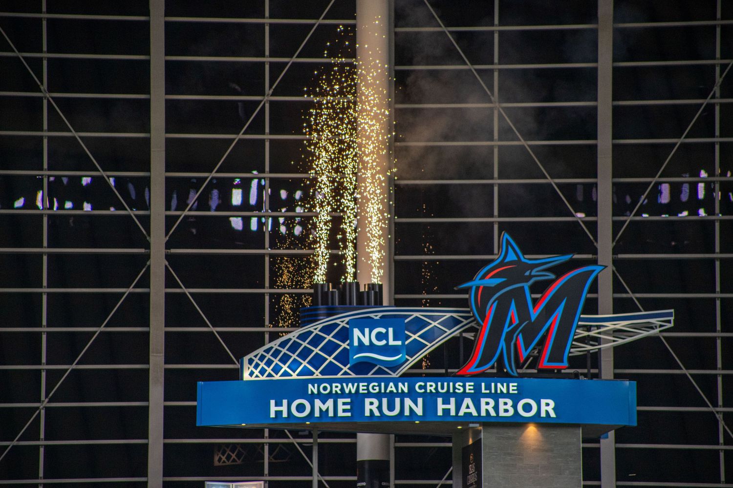 Baseball stadium interior showing illuminated signage and structural beams against dark night sky.
