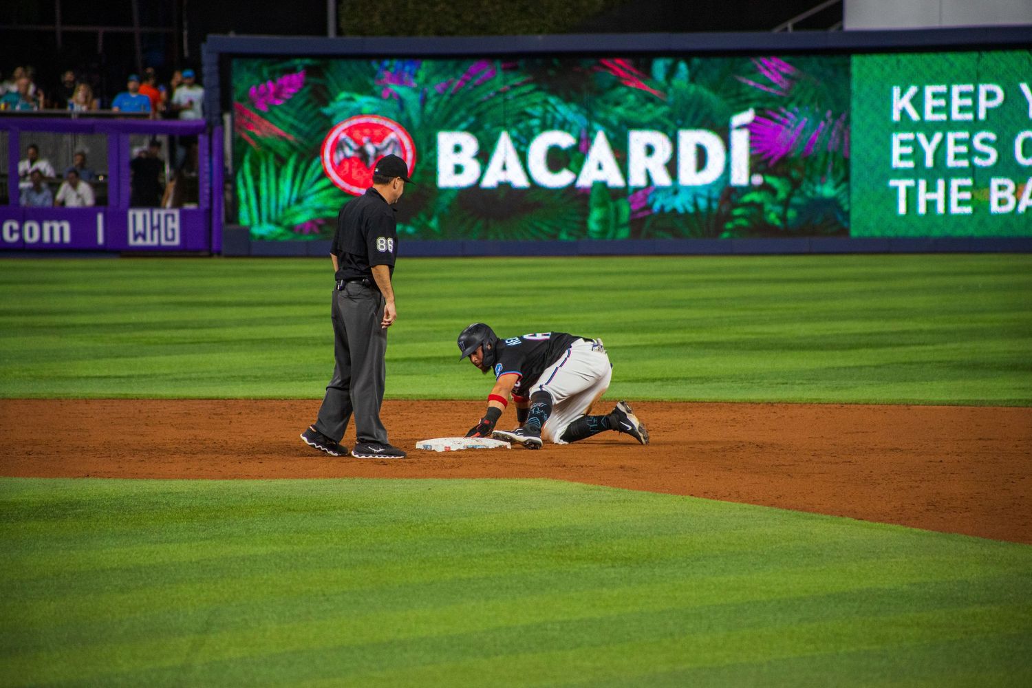 Baseball stadium at night with illuminated Bacardi advertisement visible on outfield wall.