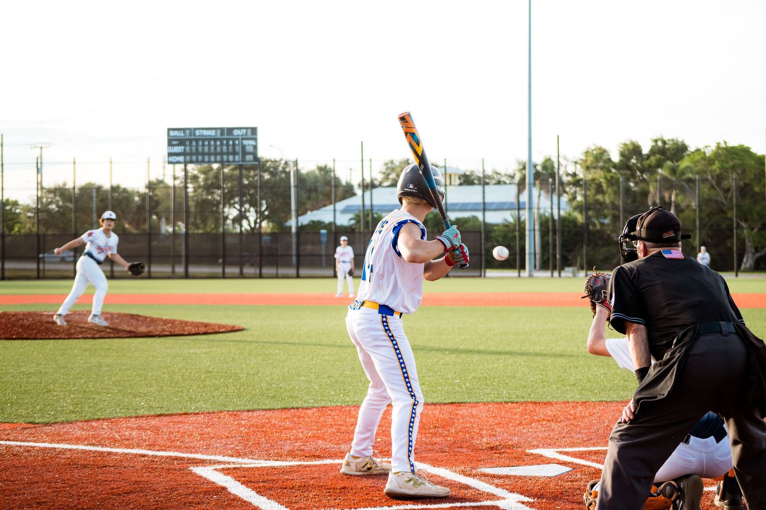 Baseball batter stands ready at home plate during daytime game with umpire and infielder in view.