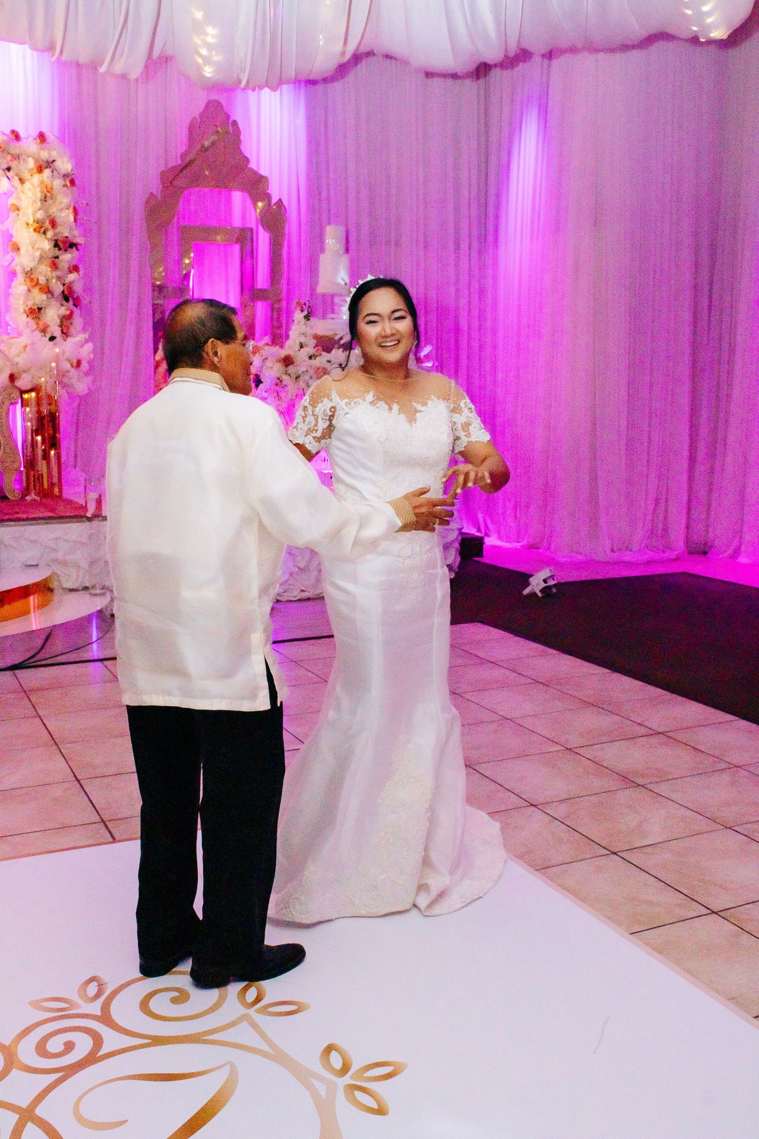Bride in white gown dances with guest in traditional barong during reception.