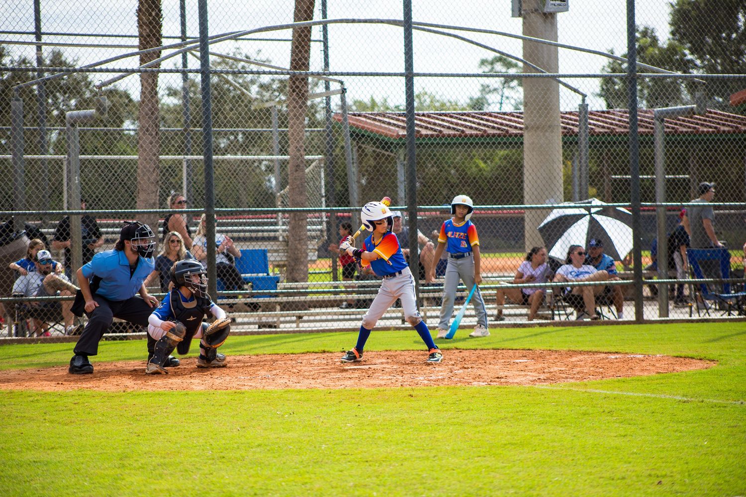 Baseball batter at the plate taking a swing during a youth game with catcher and umpire present.