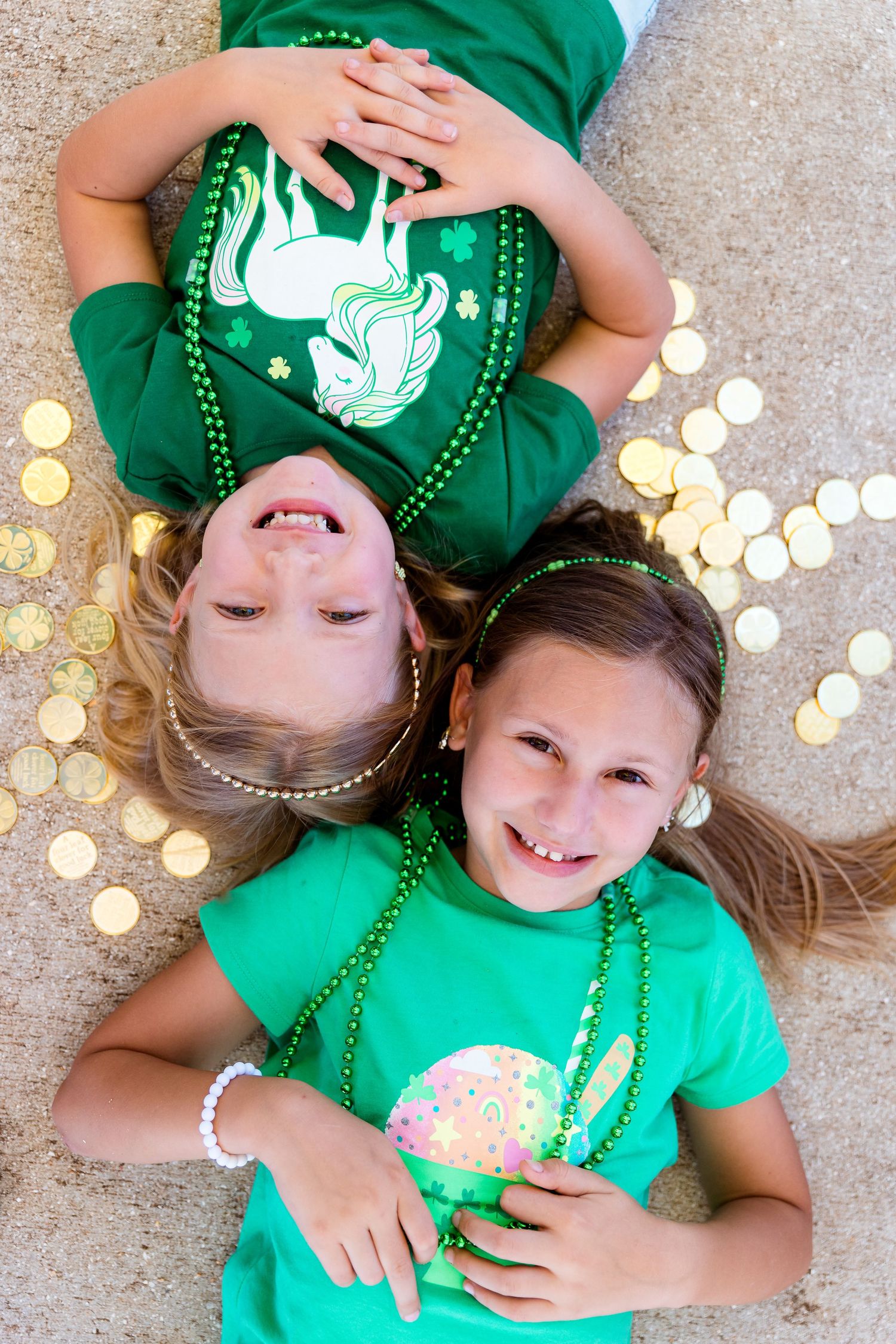 Children in green shirts with festive beads laying on ground surrounded by gold coins.