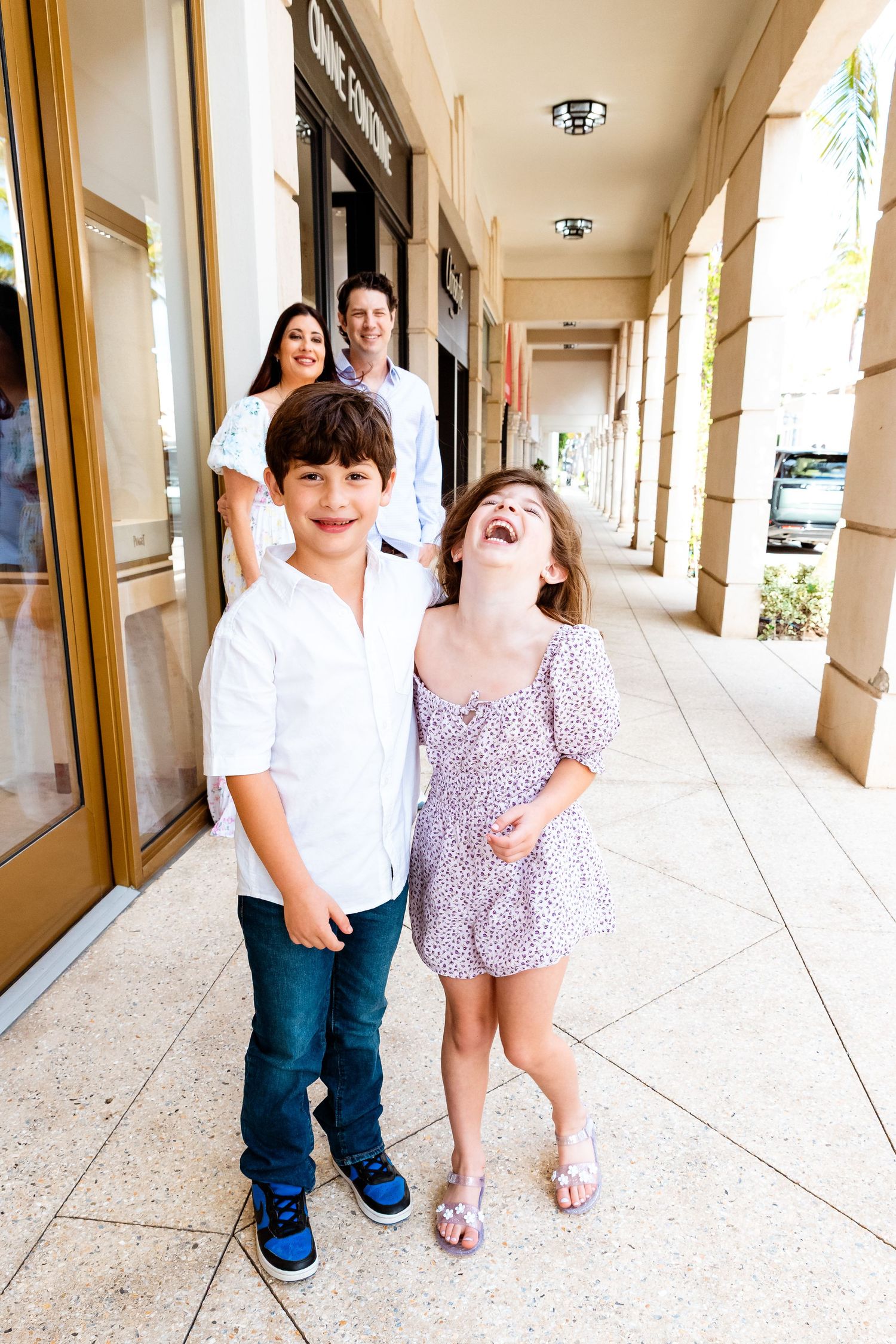 Happy family with two children laughing and posing along a covered outdoor shopping corridor.