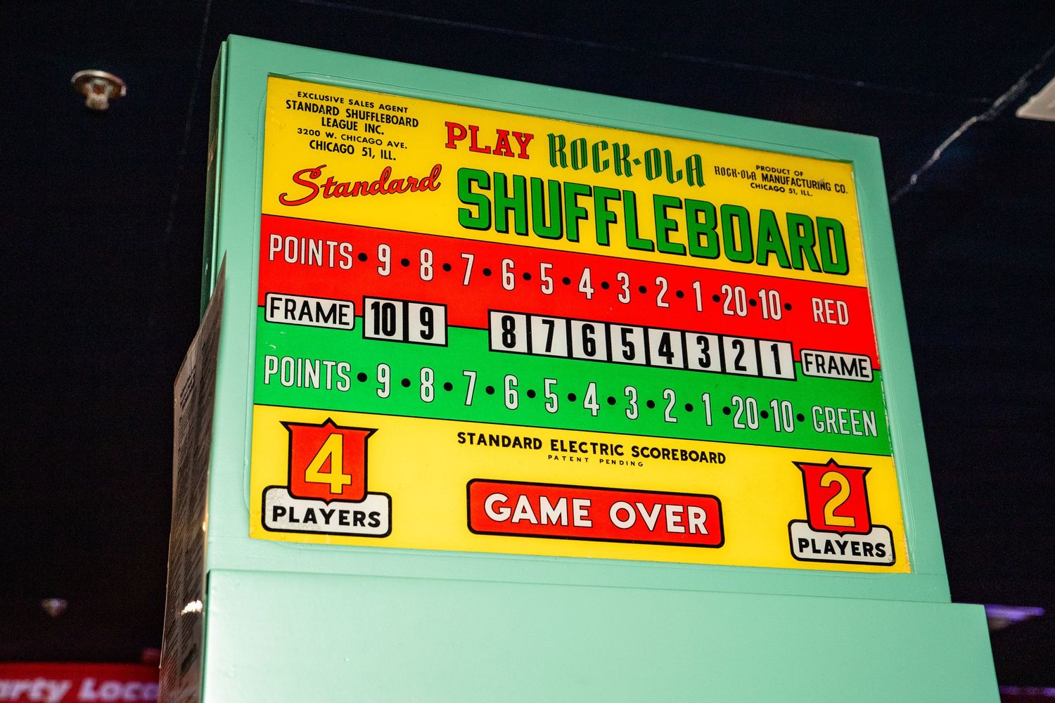 The image shows a large digital display board with scores and game information for a shuffleboard game.