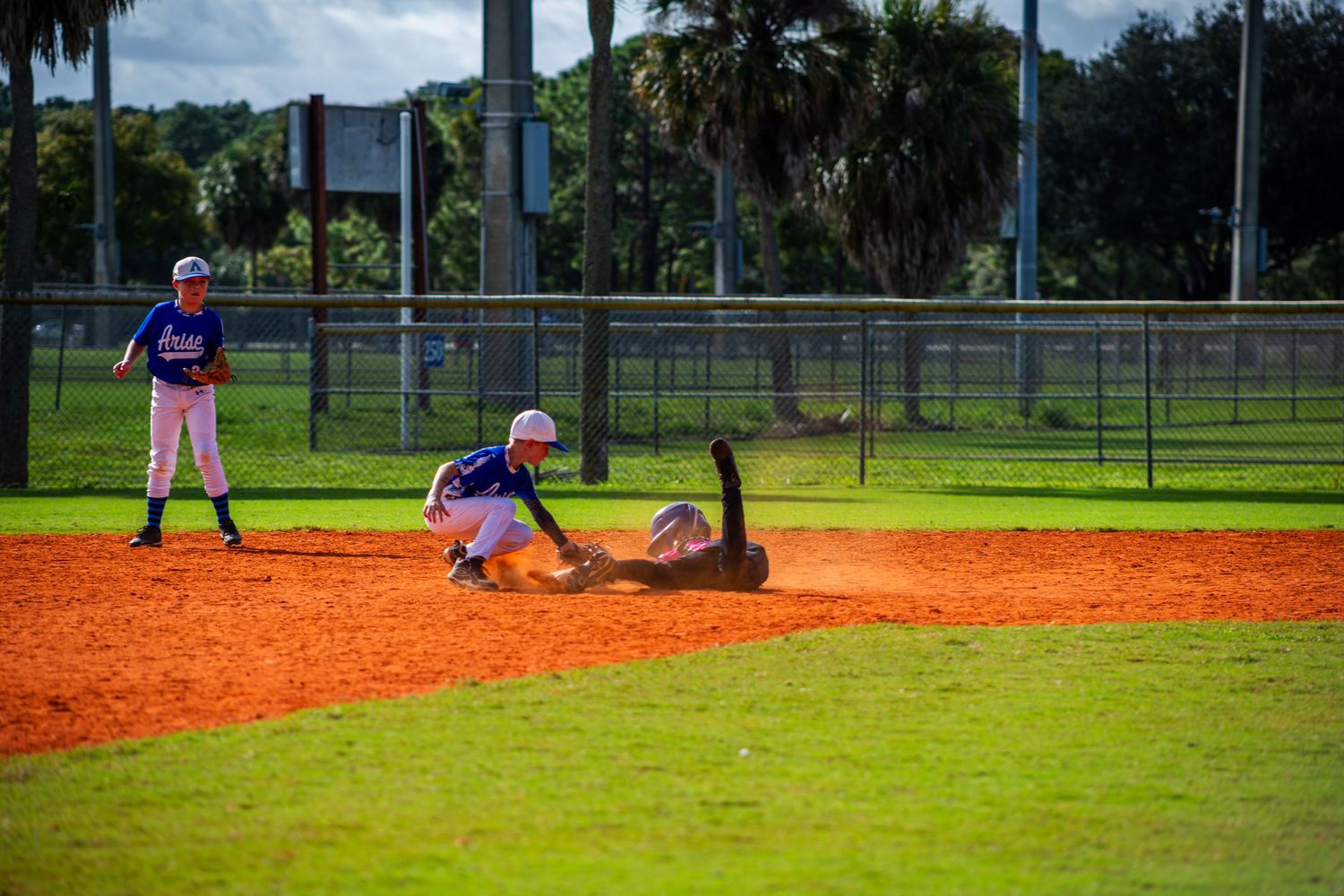 Baseball players in action during a play at third base on an orange clay infield with green grass outfield.