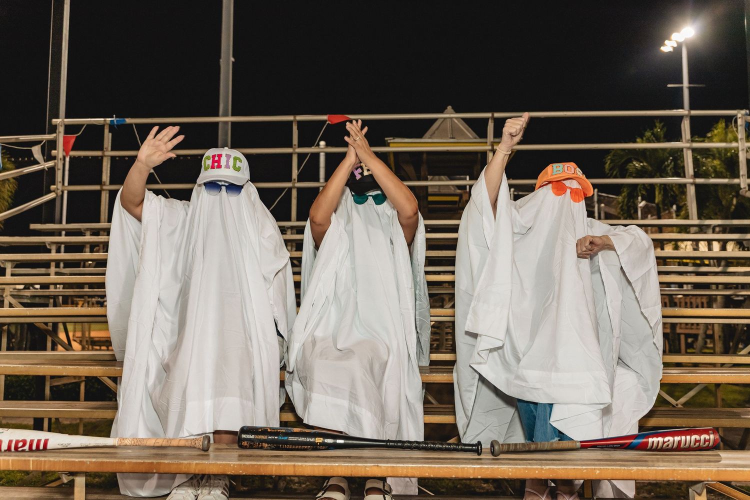 White-sheeted figures line up along baseball field bleachers under stadium lighting.