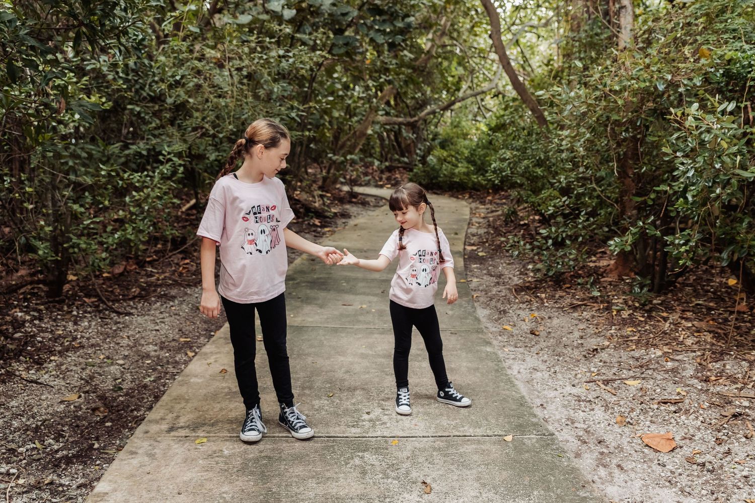 Two young friends in matching t-shirts walk together on a shaded path through lush greenery.