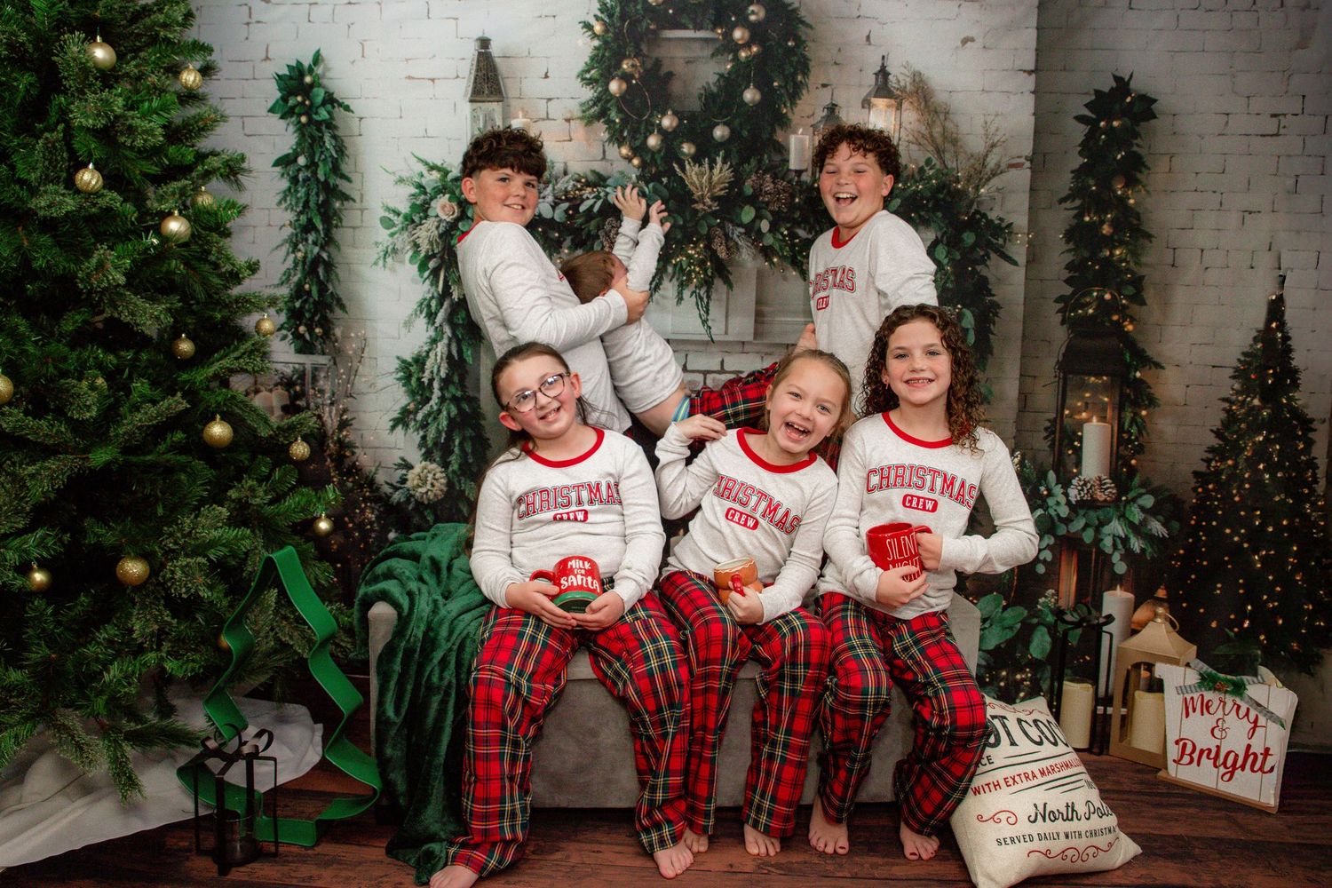 A festive holiday photo with five people in matching red plaid pajamas posing by a Christmas tree and decorations.