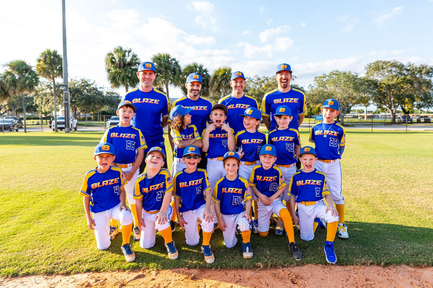 Baseball team in blue jerseys poses together on field during golden hour sunlight.