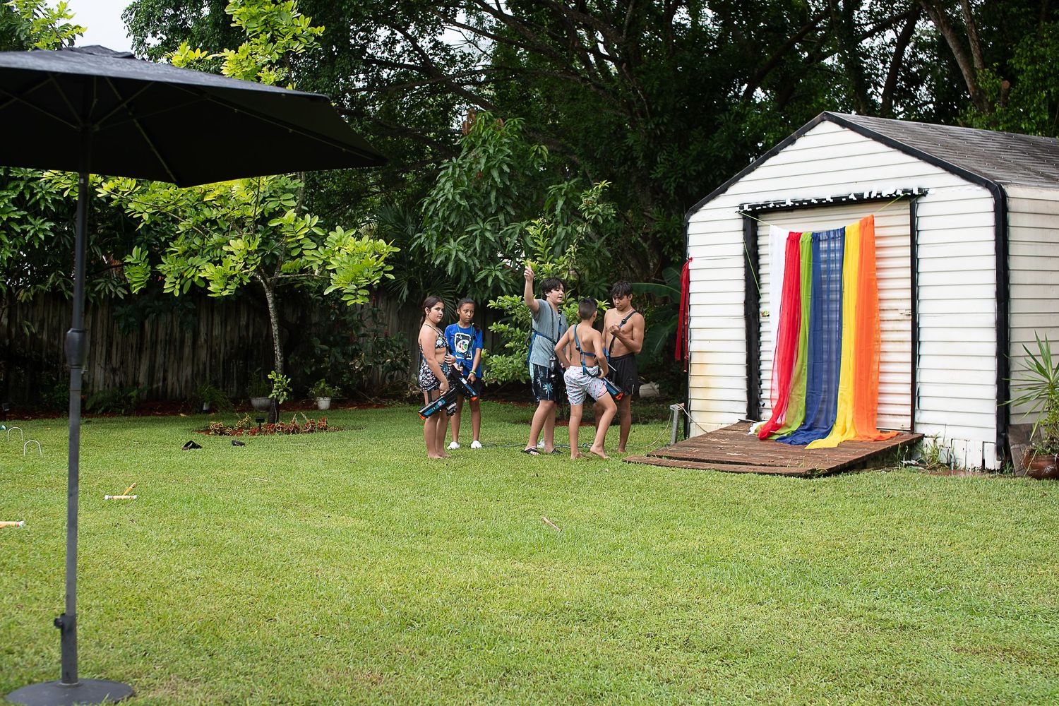 Backyard party setting with rainbow decorations on a white shed.