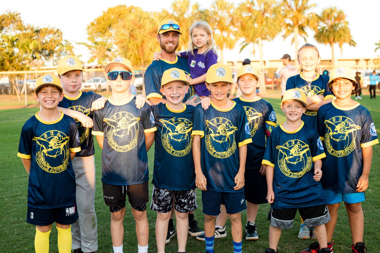 Youth sports team poses with coaches on field at sunset wearing navy team uniforms.
