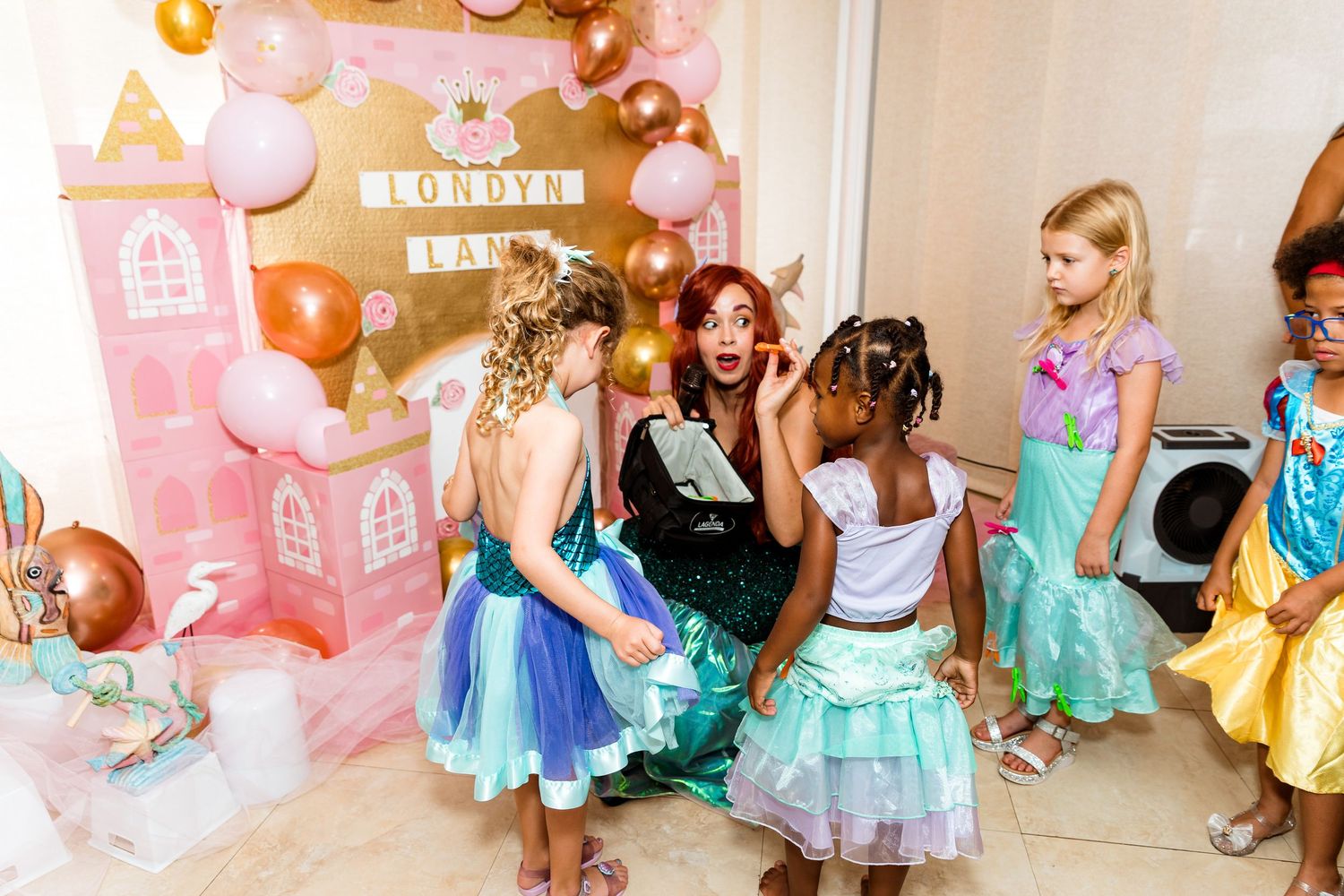 Young guests in colorful princess dresses dancing at a themed birthday party with balloon decorations.