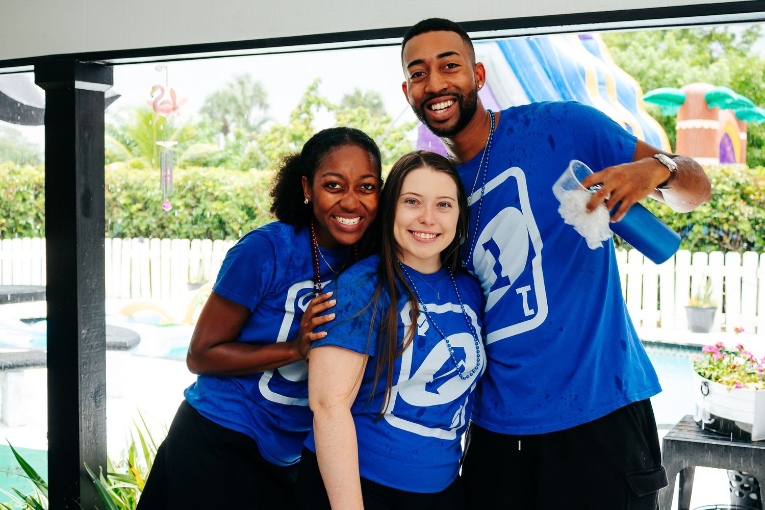 Three people wearing matching blue Spartan logo t-shirts smile together at an outdoor event.
