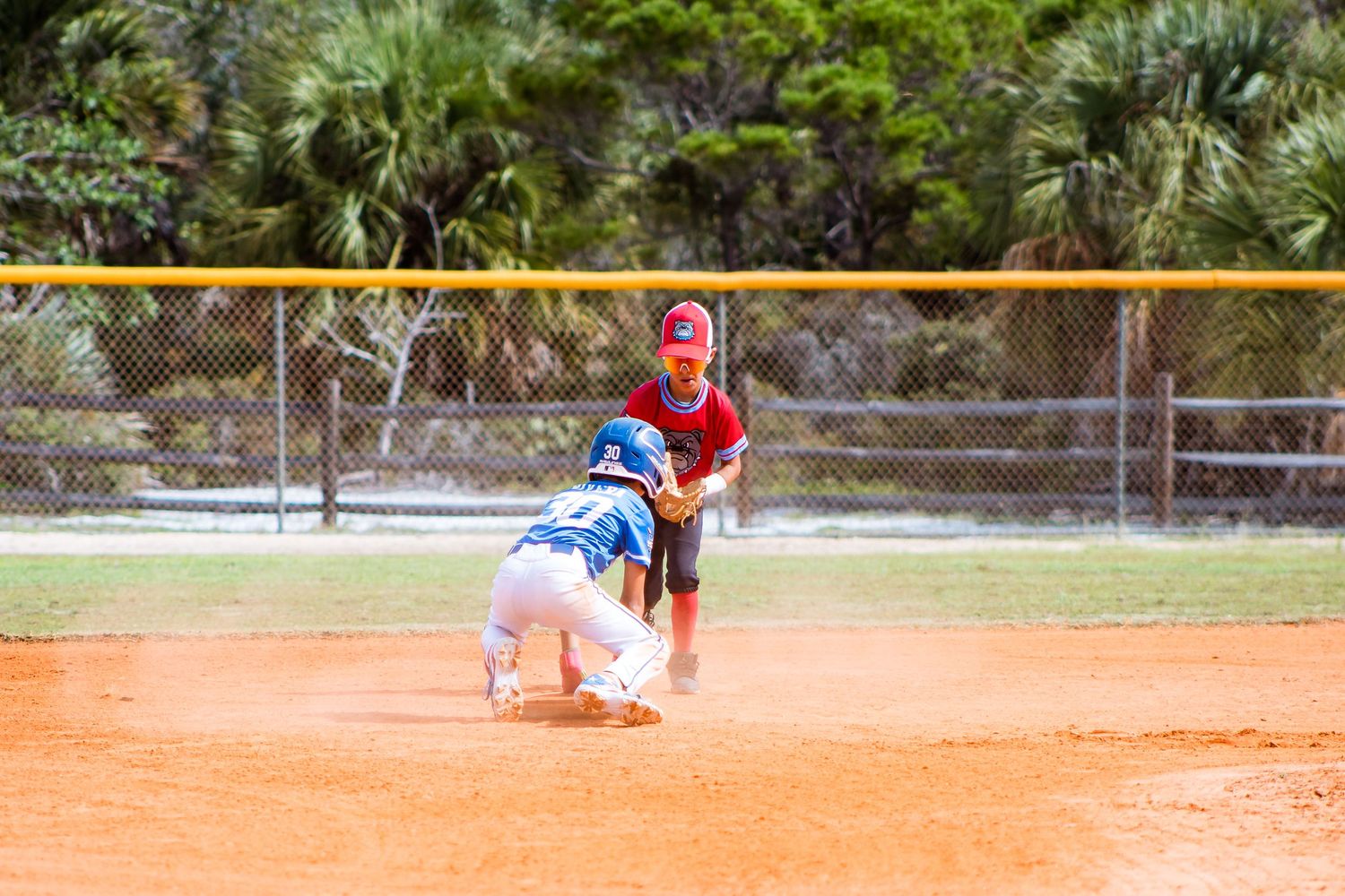 Baseball players practice fielding drills on an orange clay infield during a training session.