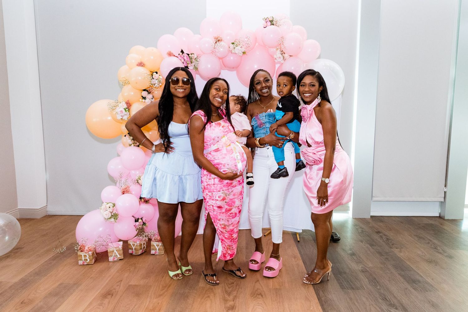 A celebratory group photo with a pink balloon arch background.