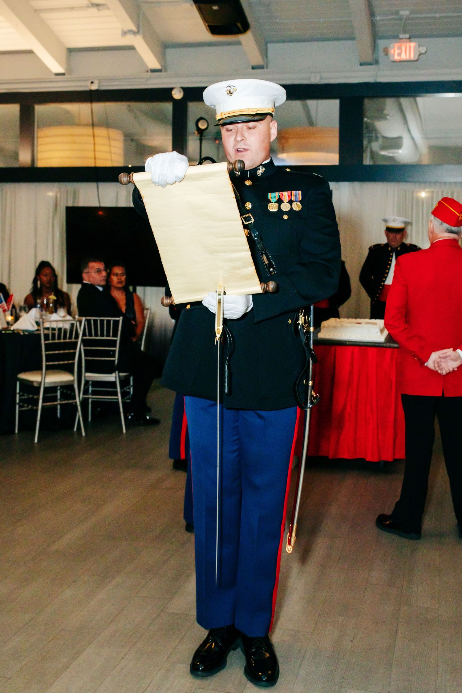 Marine in dress uniform reads from a ceremonial script during a formal event.