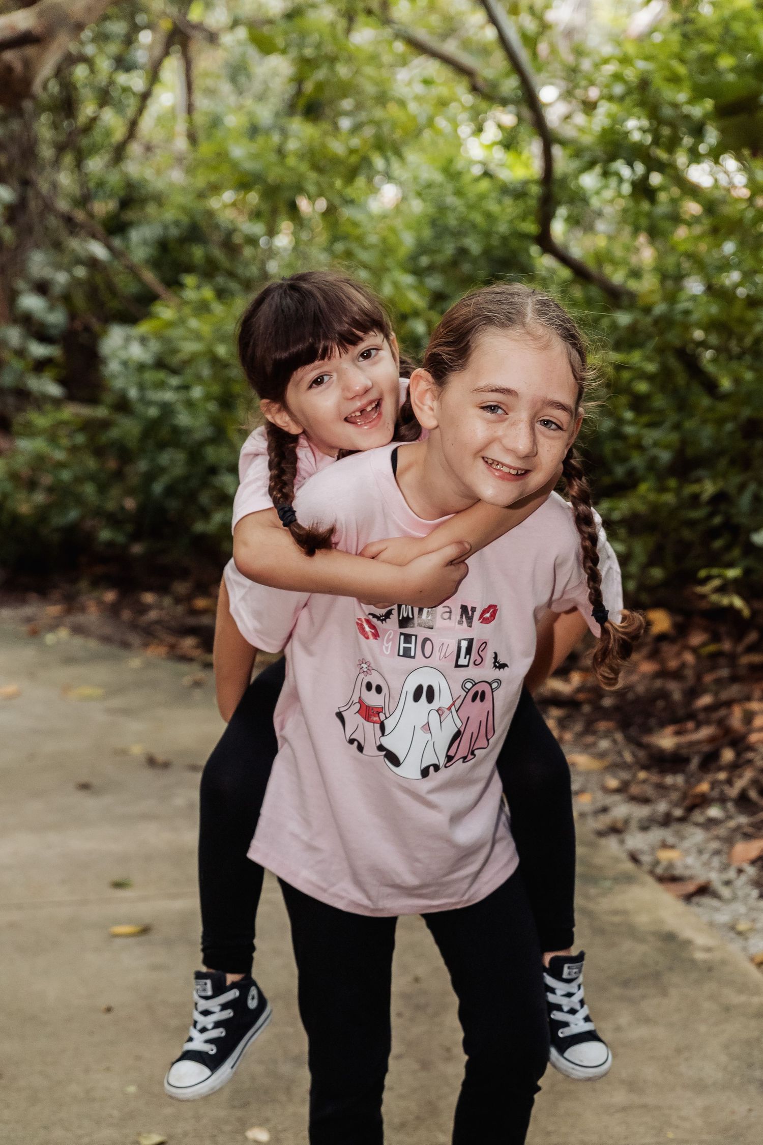 Two children playing and laughing together outdoors while giving piggyback rides in matching pink and black outfits.