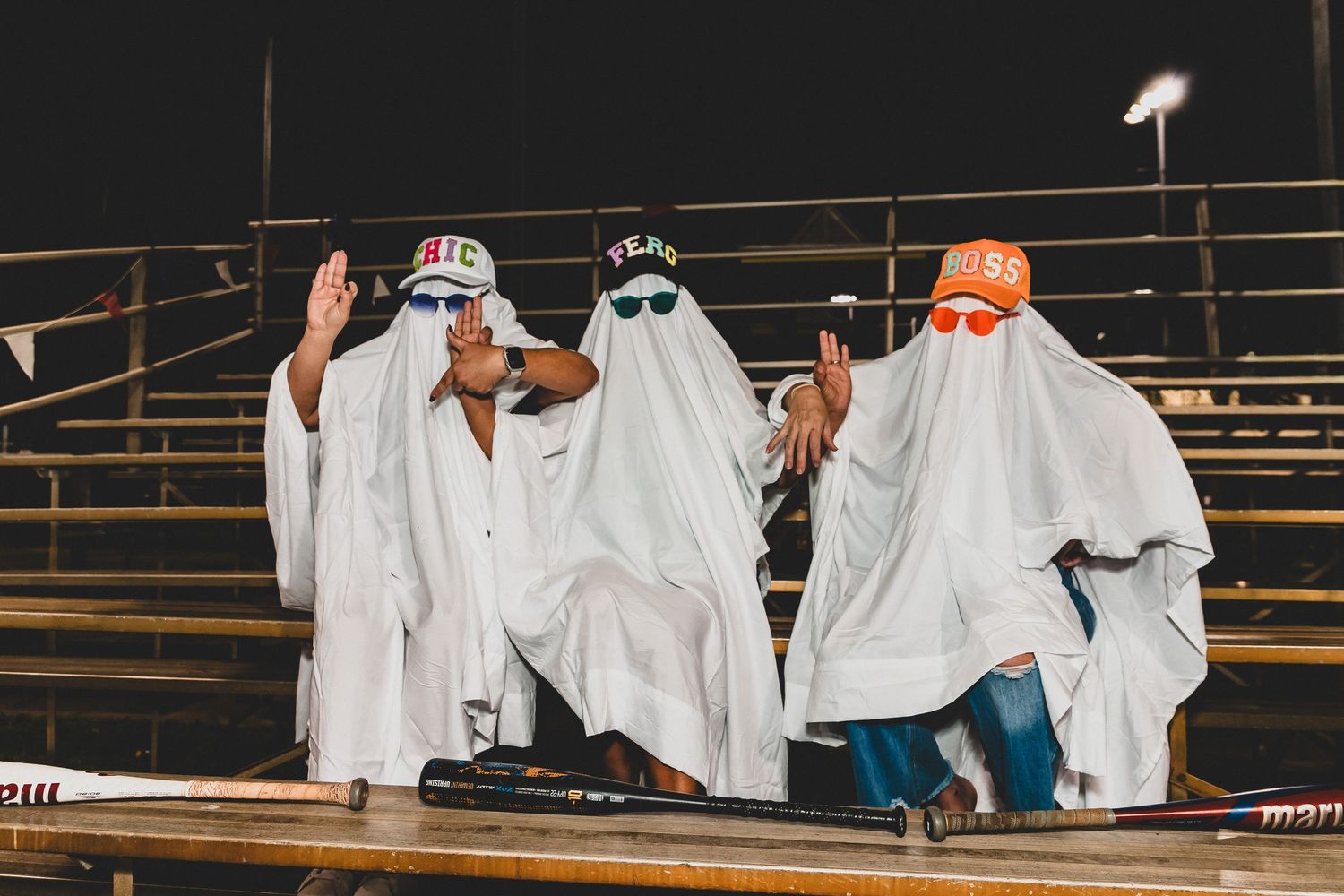Line of spectators in white sheets perform coordinated movements on bleachers under stadium lights.