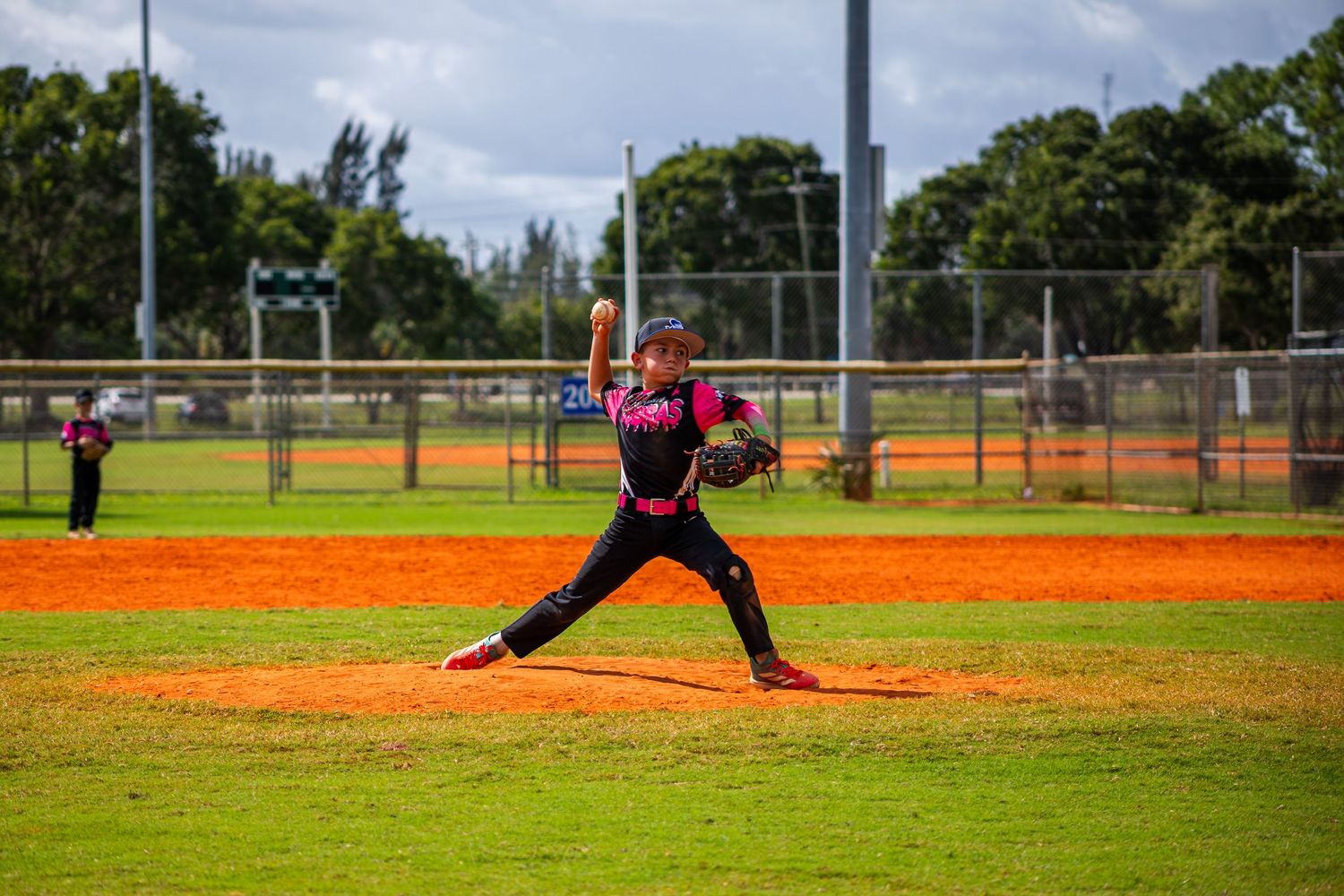 A baseball pitcher in pink and black uniform follows through on their delivery motion during a game.
