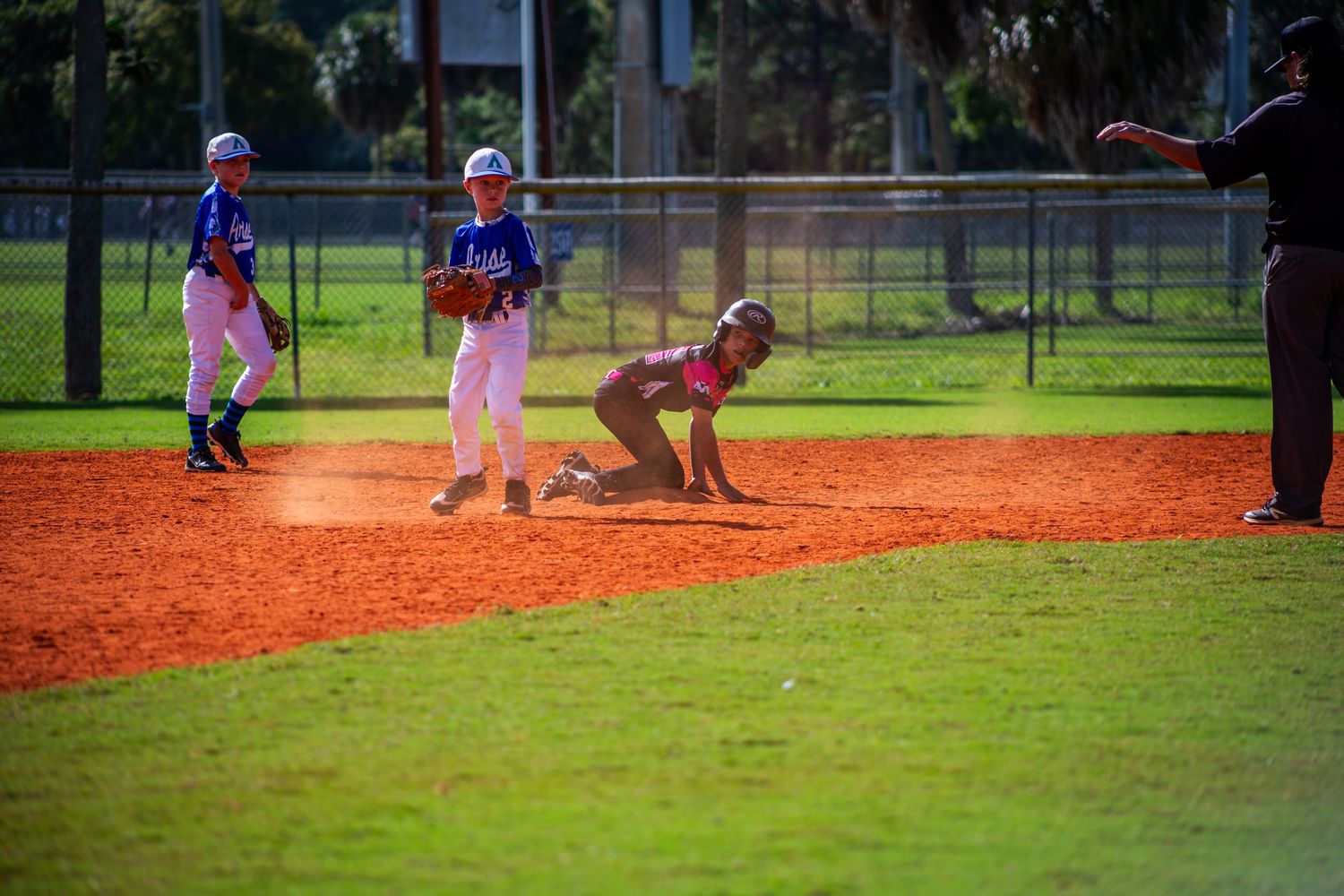 Youth baseball players practicing on a red clay baseball field during a sunny day at a sports complex.