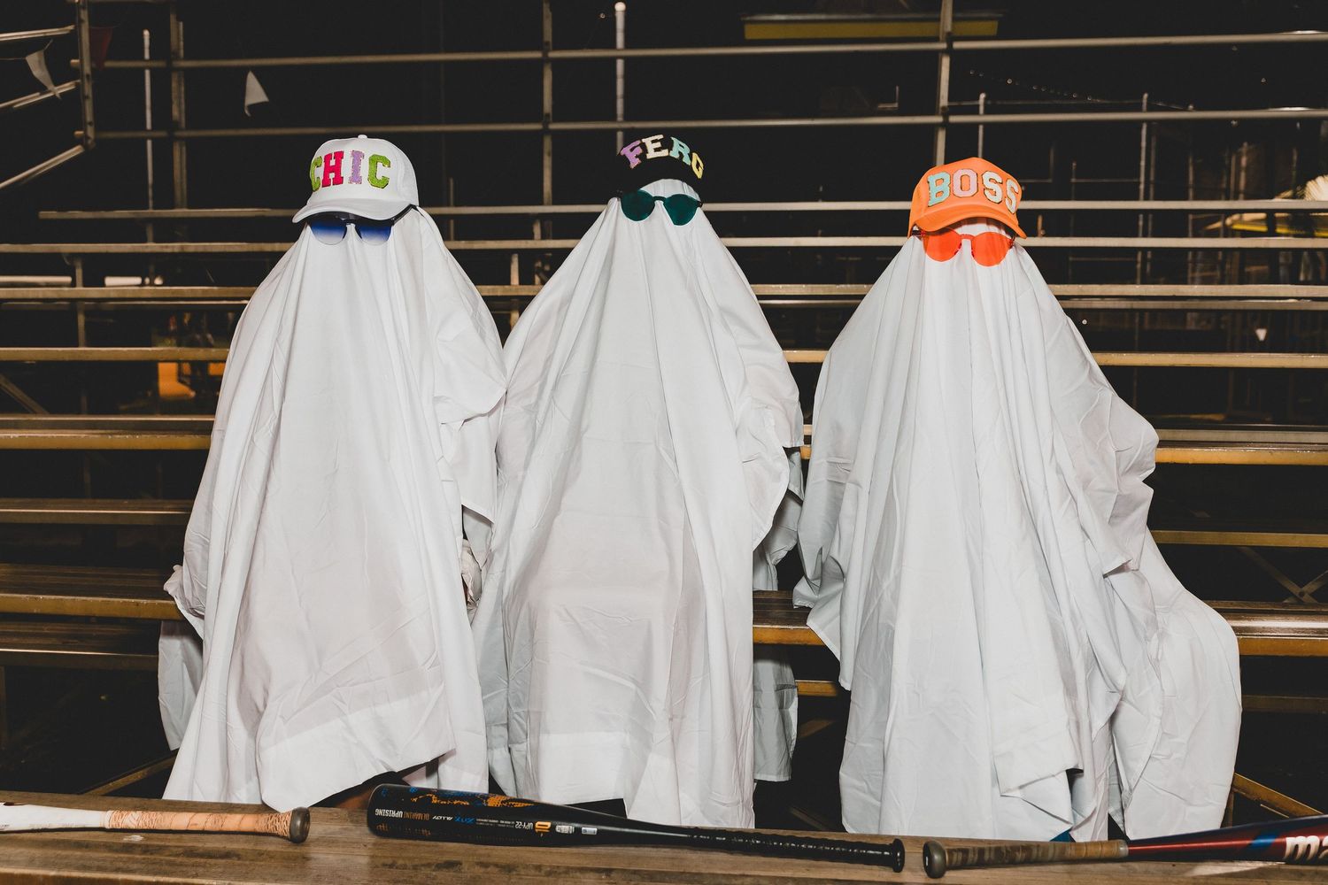A row of people dressed as ghosts in white sheets sitting on wooden bleachers at night.
