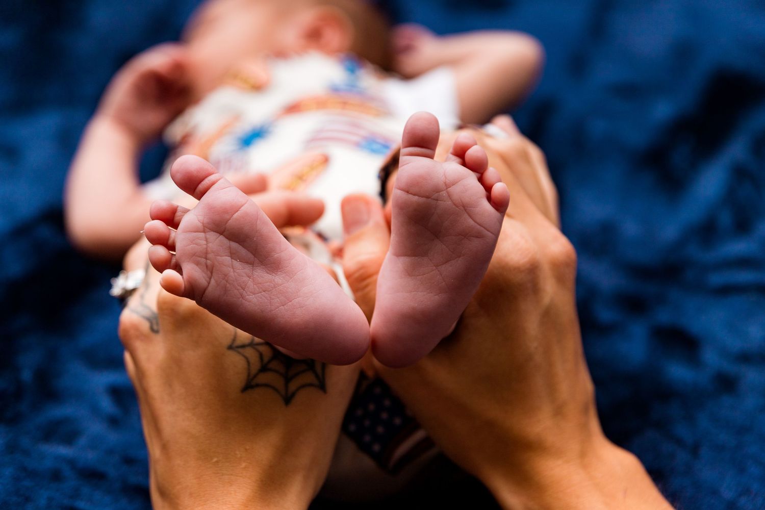 Adult hands gently hold tiny newborn baby feet against a dark blue textured background.