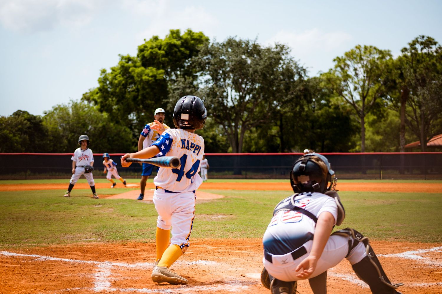 Baseball player at bat in white uniform with yellow socks stands ready at home plate while catcher crouches behind plate.