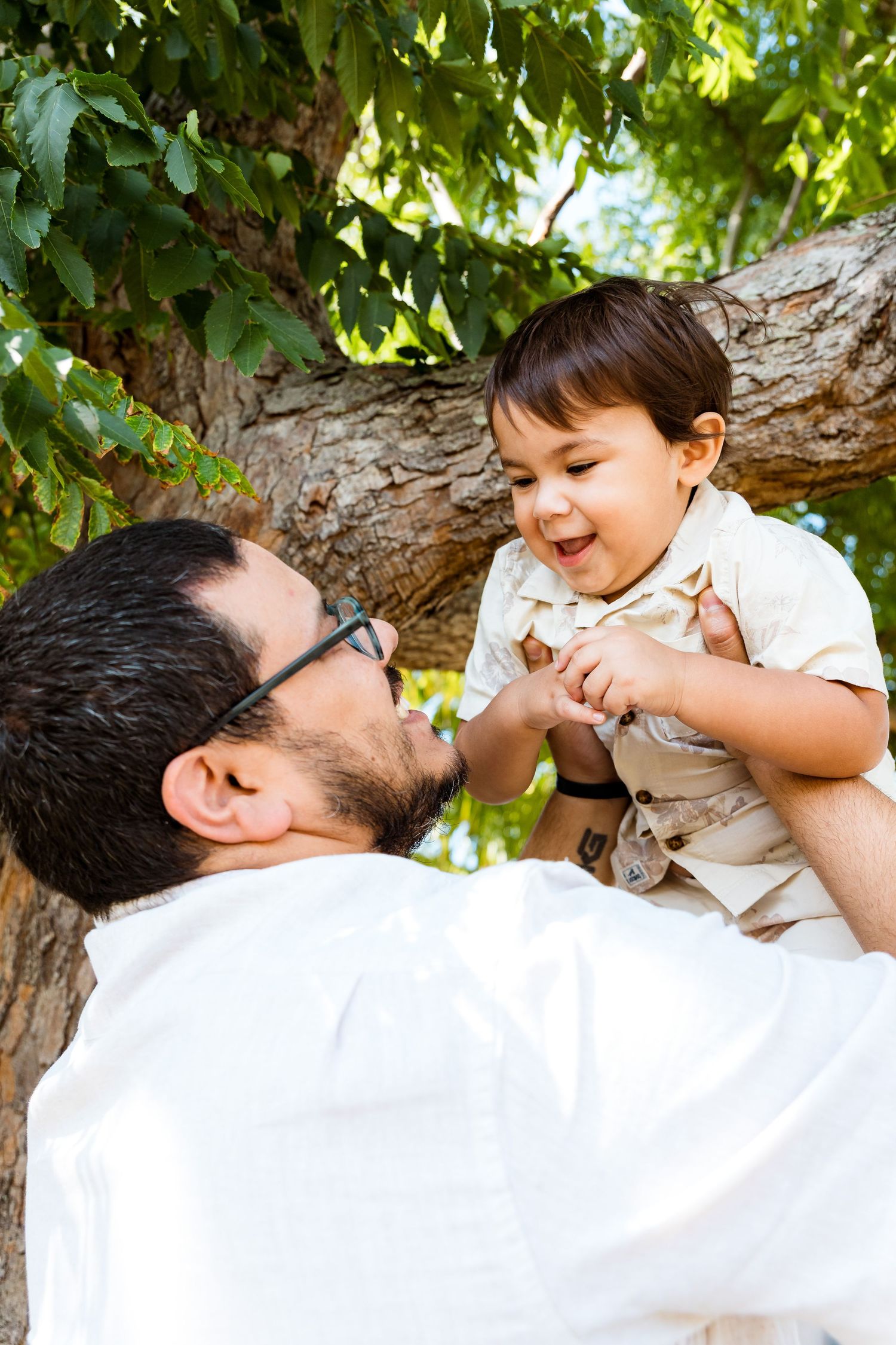 Joyful candid interaction between adult and child outdoors near a large tree branch.