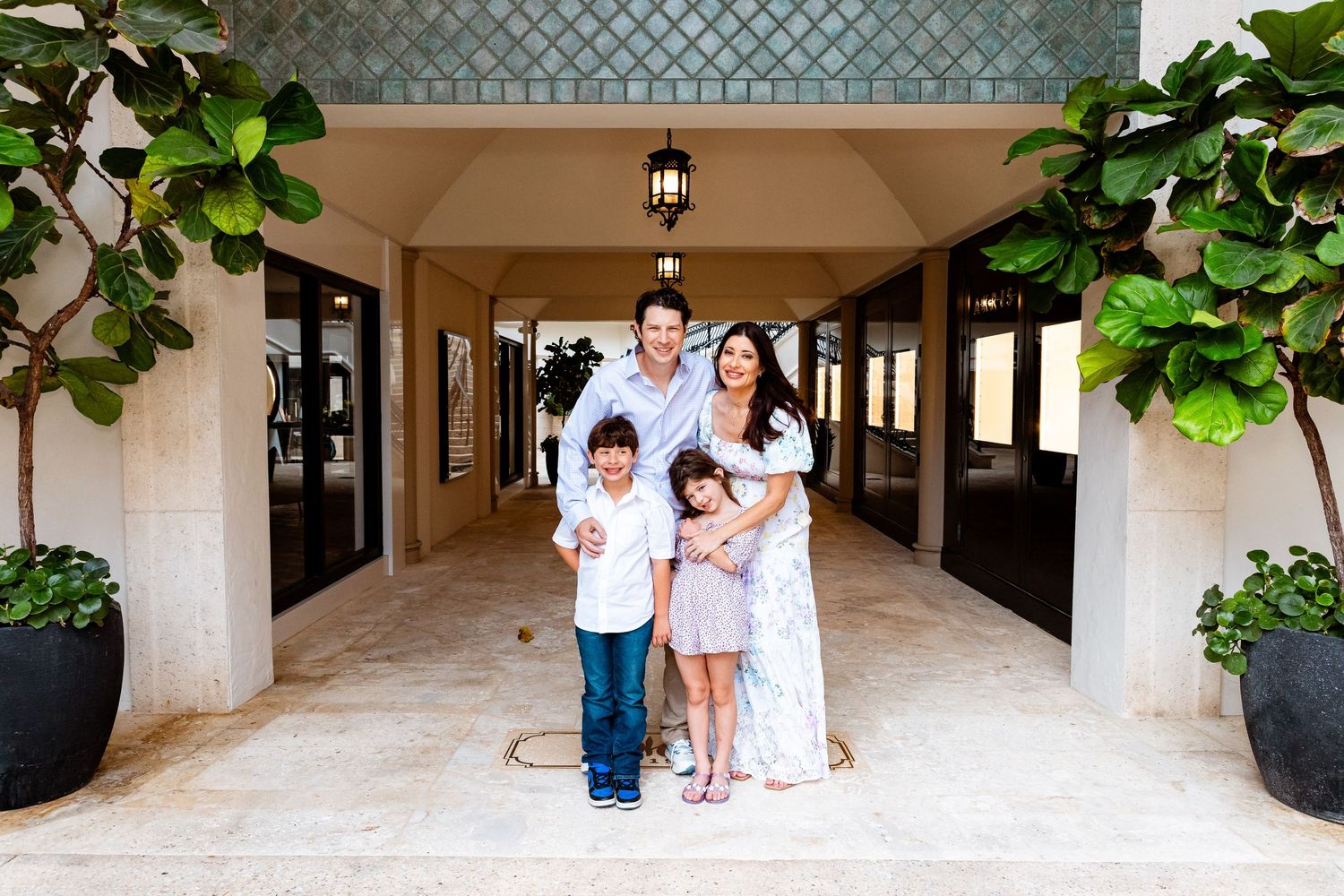 Family of four posing together under an elegant archway entrance surrounded by tropical plants.