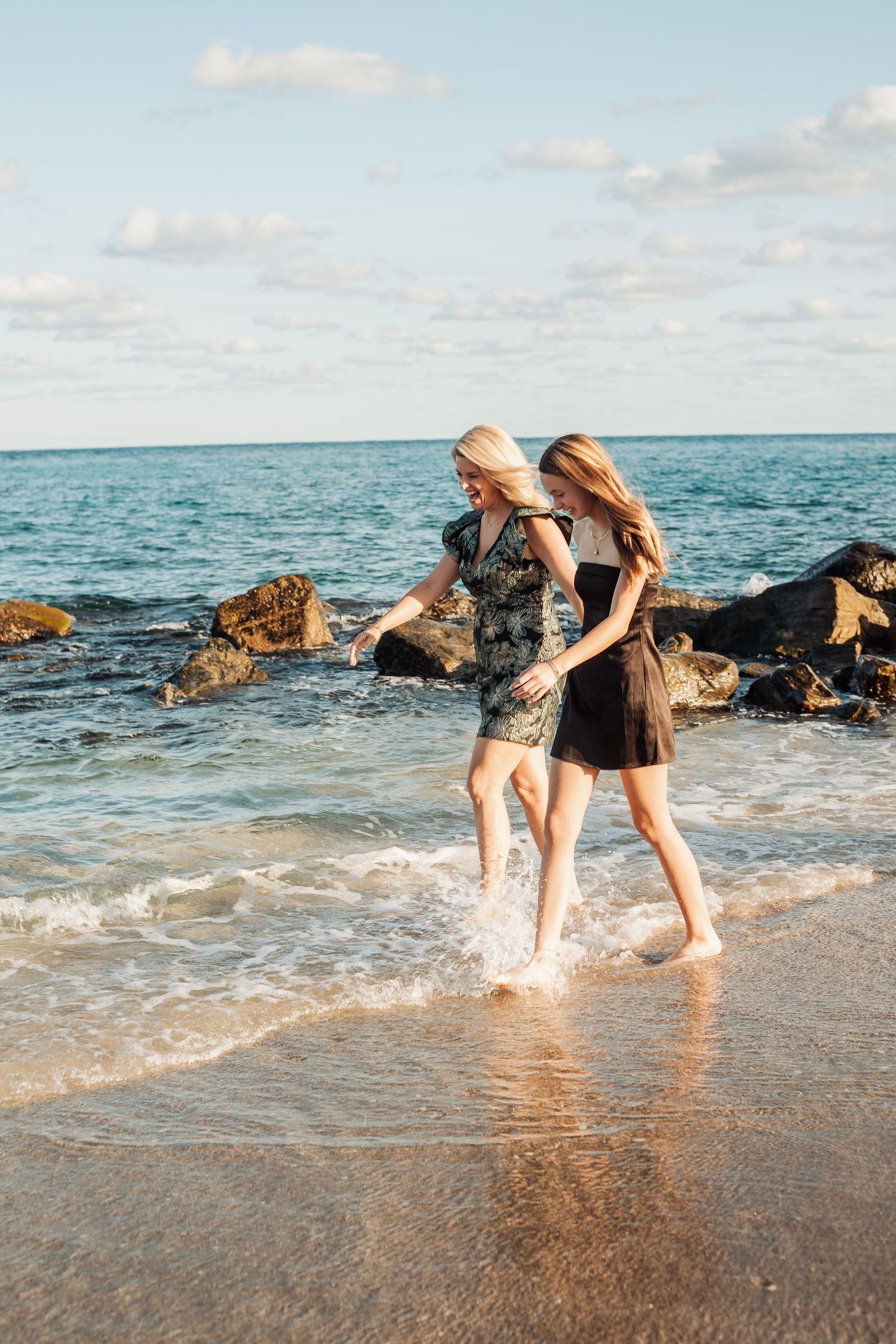 Friends enjoying sunset walk together along ocean shore with waves lapping at their feet.