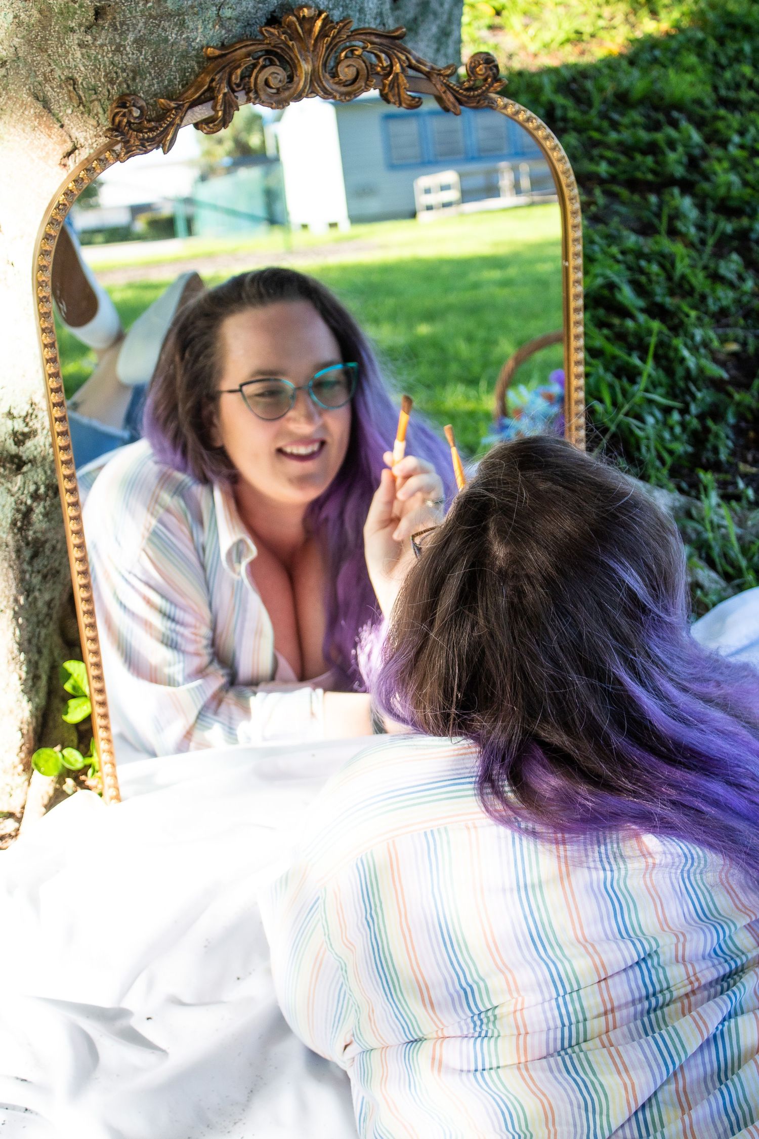 Reflection in an ornate gold mirror shows artist working on outdoor art project.