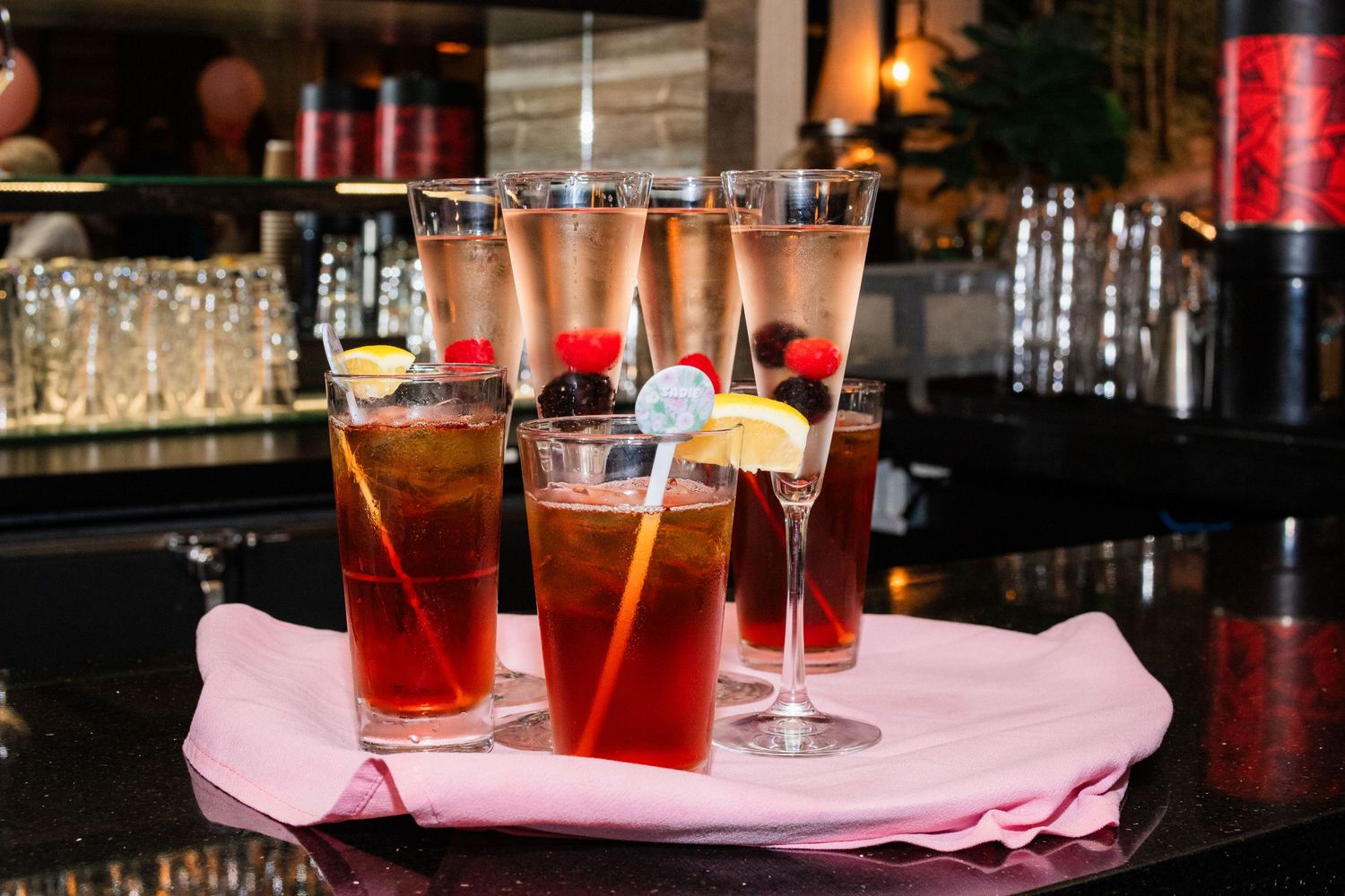 Assorted cocktails and beverages arranged on a pink napkin at a bar.