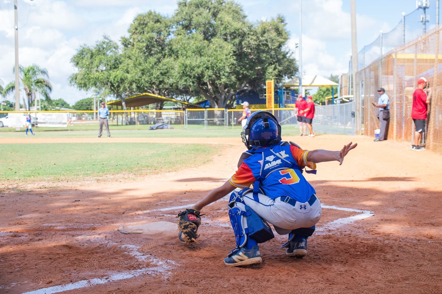 A baseball catcher crouches behind home plate in protective gear during a youth game.