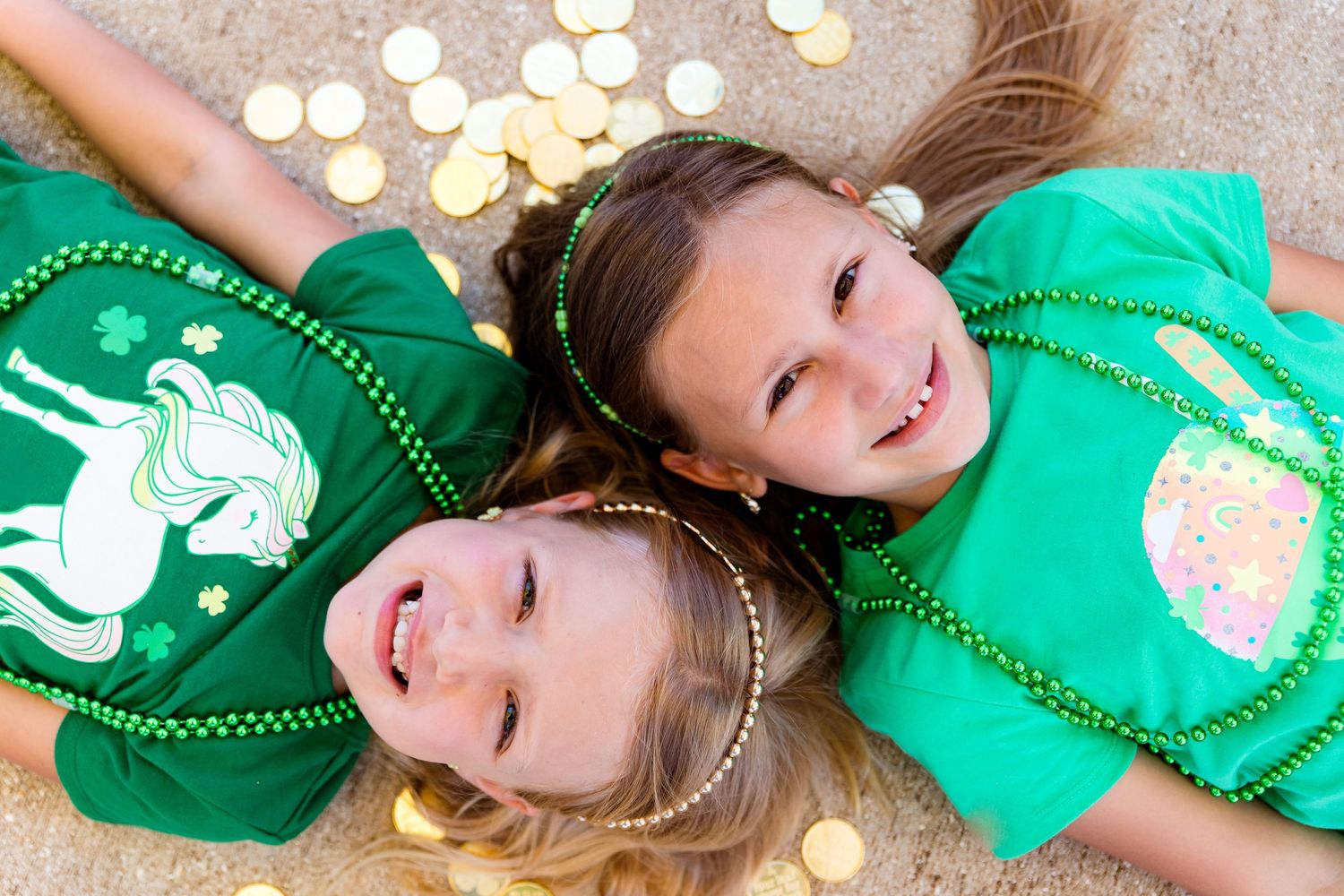 Two children laying on ground wearing matching green shirts with decorative gold coins.