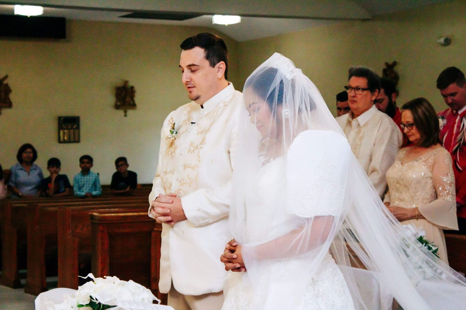Traditional church wedding ceremony with bride in white veil and groom in light colored suit at the altar.