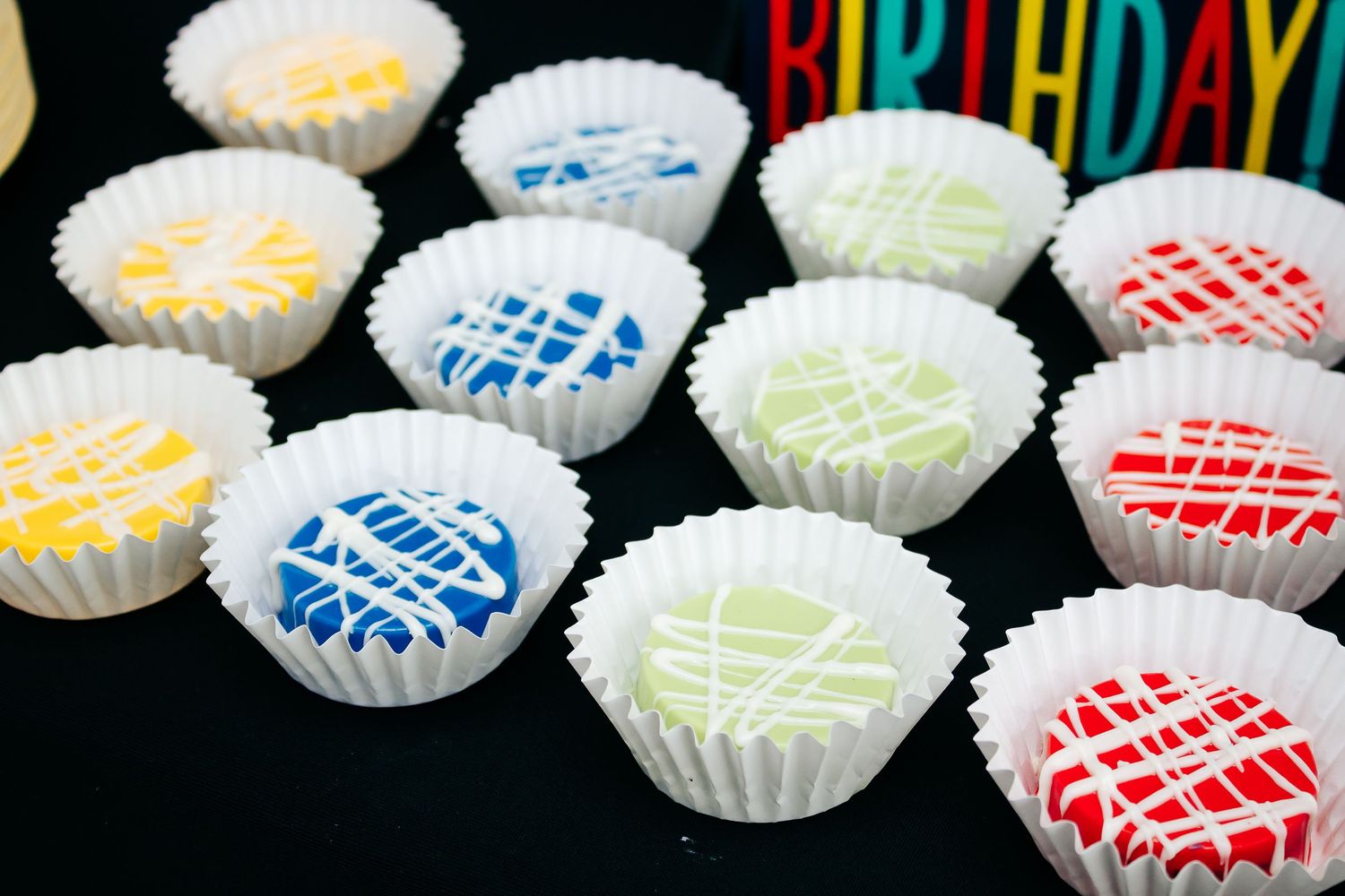 Colorfully decorated cupcakes with drizzled icing patterns in various colors on a black background.