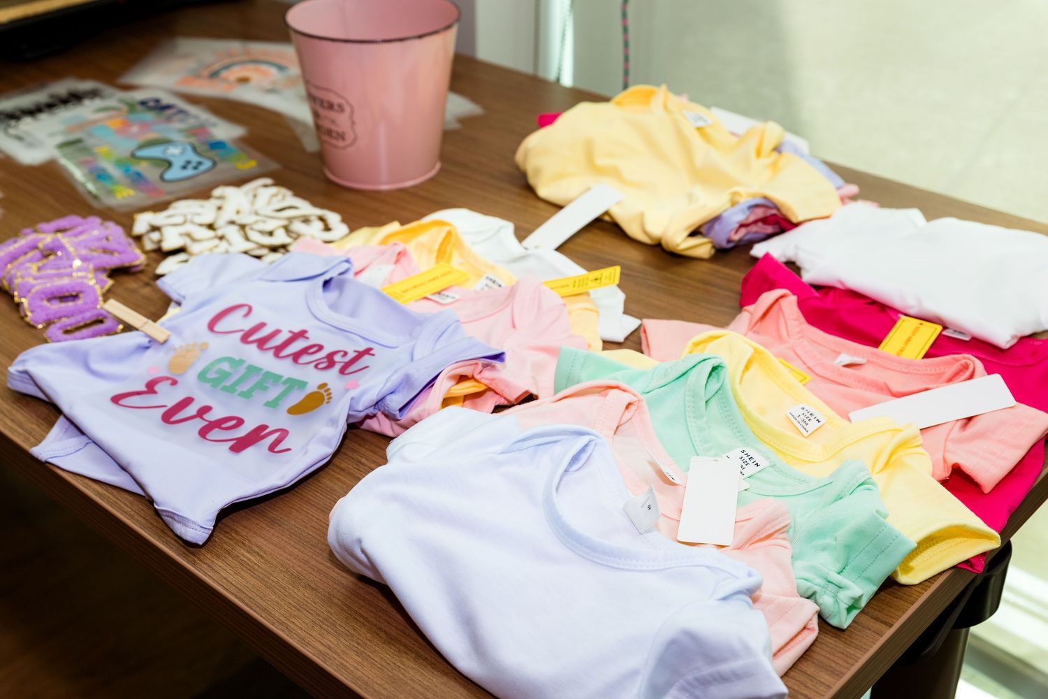 Colorful baby onesies and infant clothing items displayed on a table for customization.