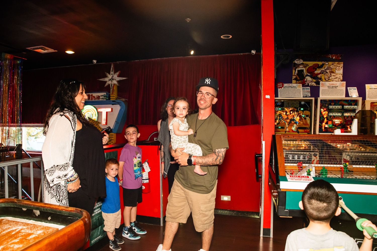 A family enjoying an evening at an arcade, with adults and children playing games and interacting together.