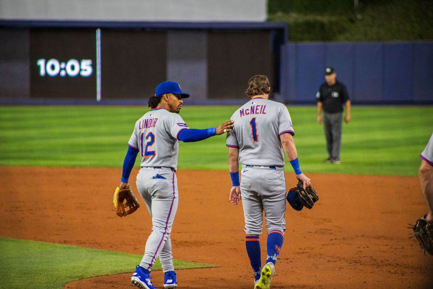 Two baseball players in grey uniforms interact on field during evening game.