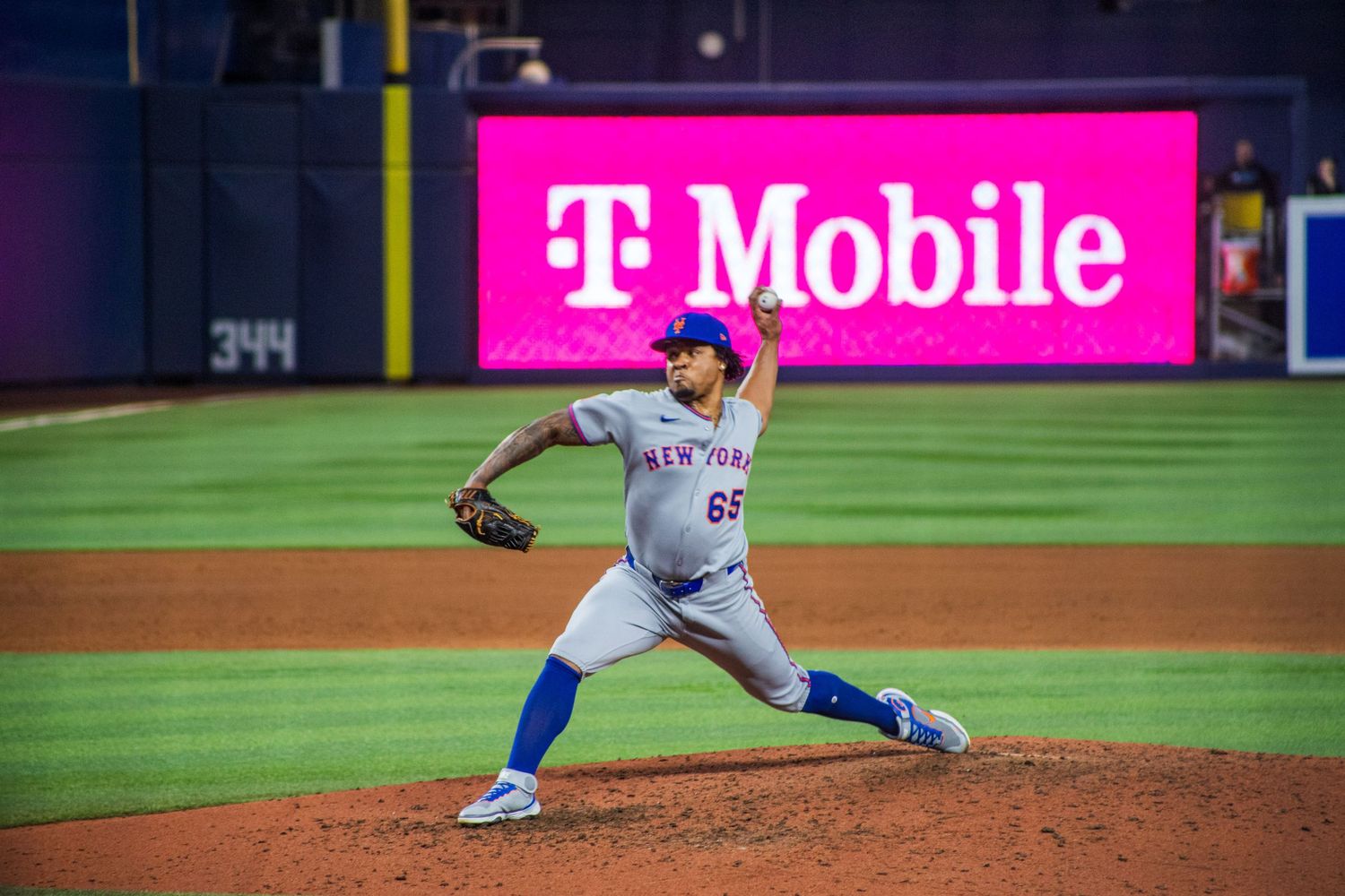Baseball pitcher in mid-throw motion on mound with T-Mobile signage visible.