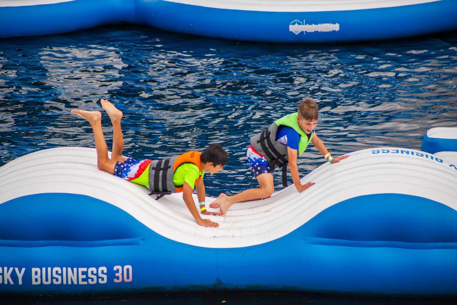 People enjoying a blue inflatable obstacle course and water activity park on a sunny day.