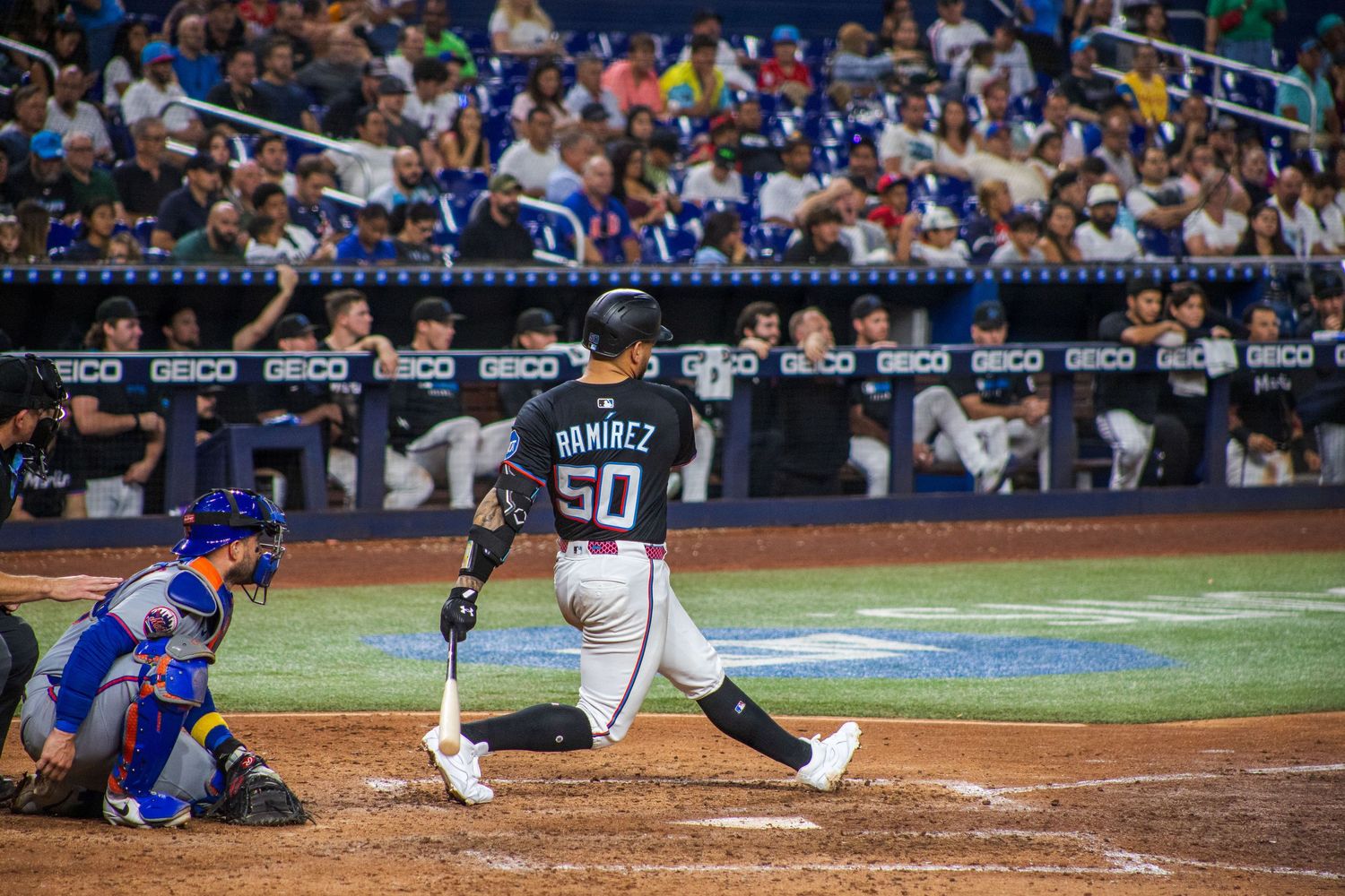 Baseball players in action during night game with crowd visible in background.