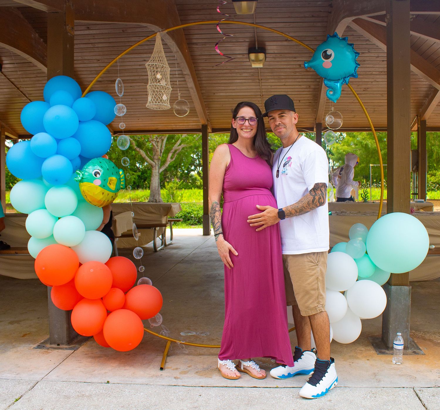 Couple standing under a pavilion decorated with colorful balloon garlands.