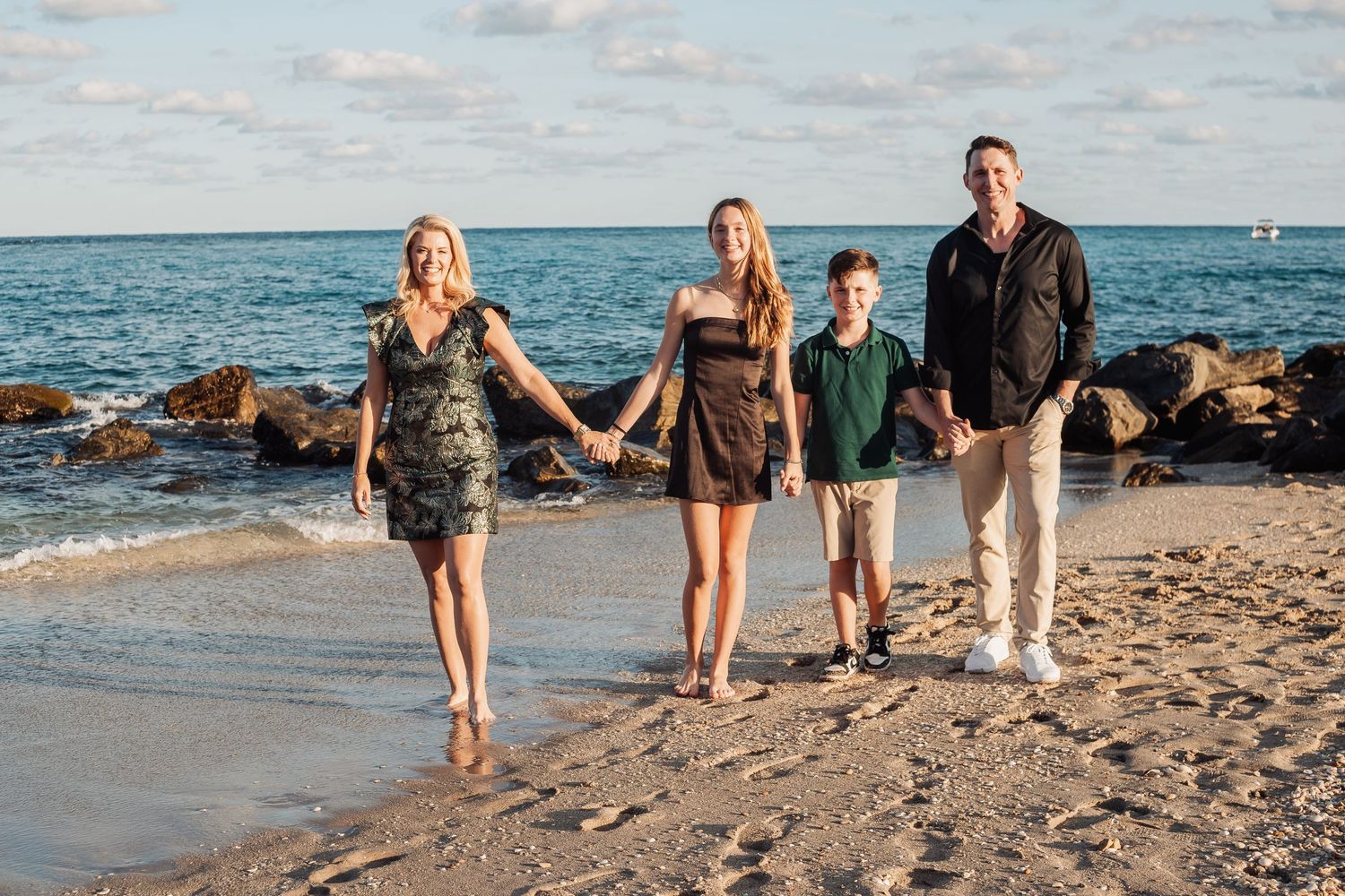 Family walking hand in hand along shoreline with turquoise ocean and rocky coast views.